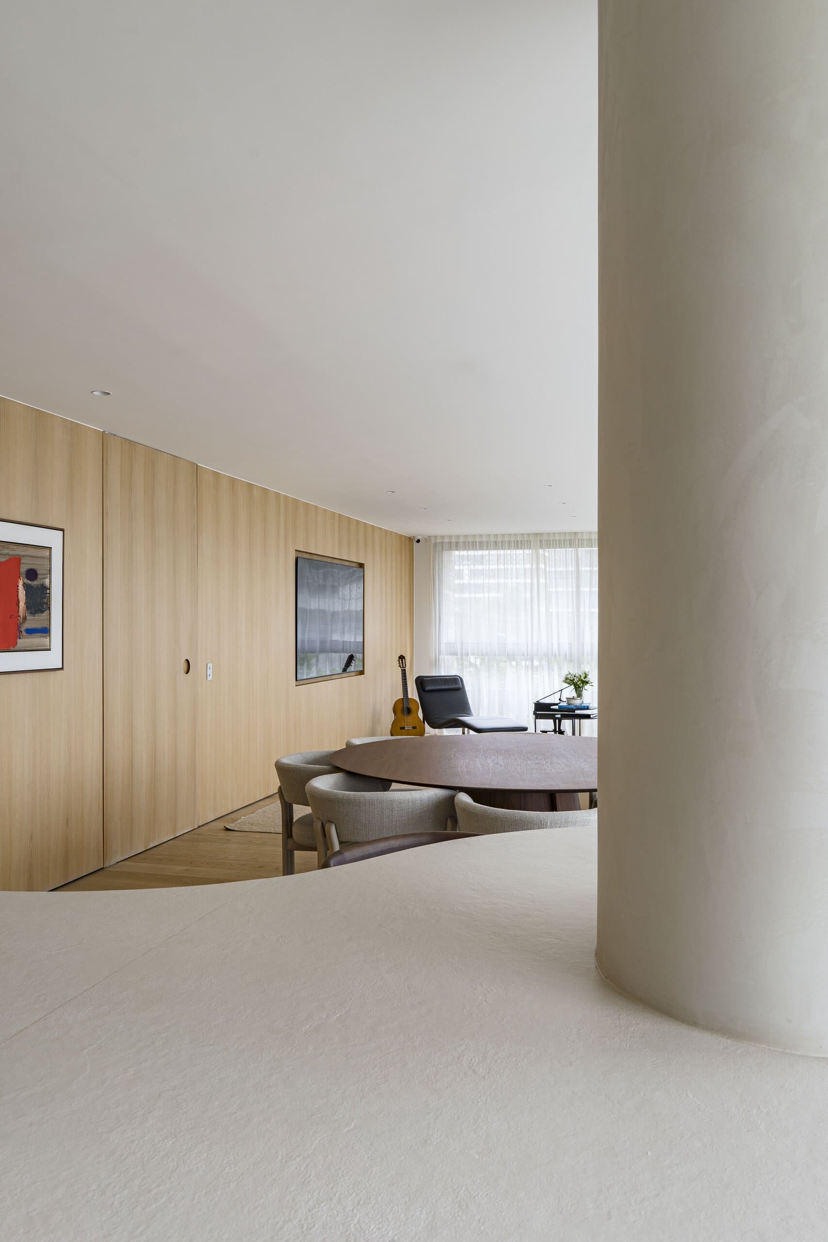 A plaster column rising from the curved island, the dining table and oak wall with framed prints beyond.