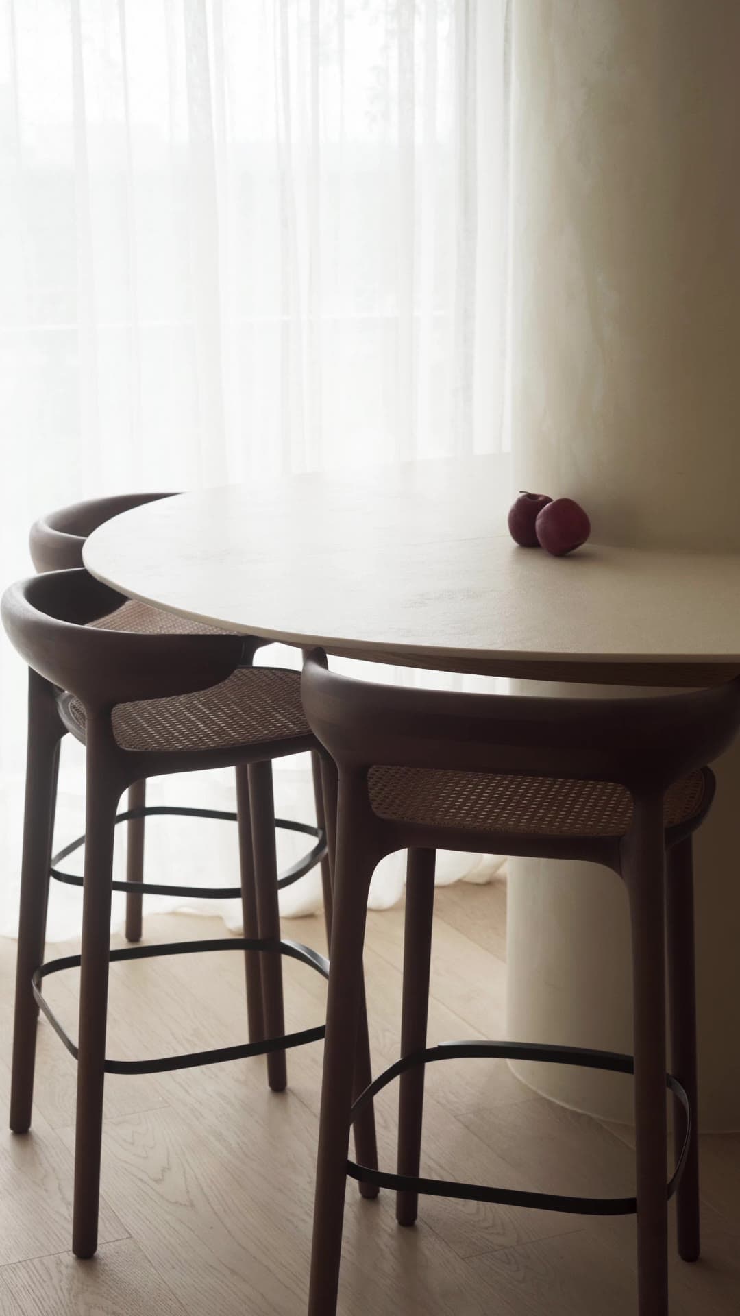 APT JM — a vertical film: cane-backed stools at the round stone table by the curtains.