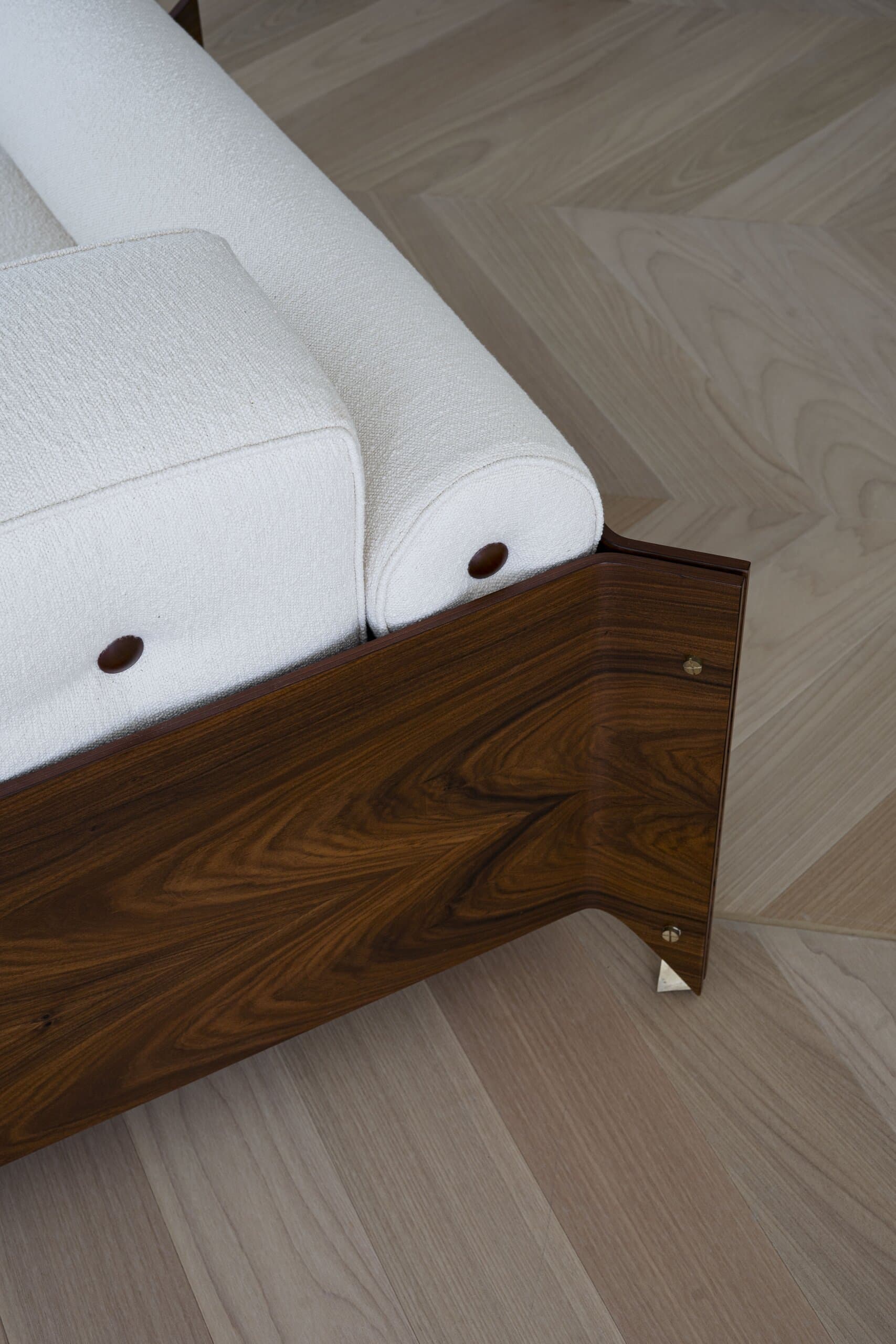 Detail: a white bouclé cushion and bolster resting on a rosewood frame over a herringbone floor.
