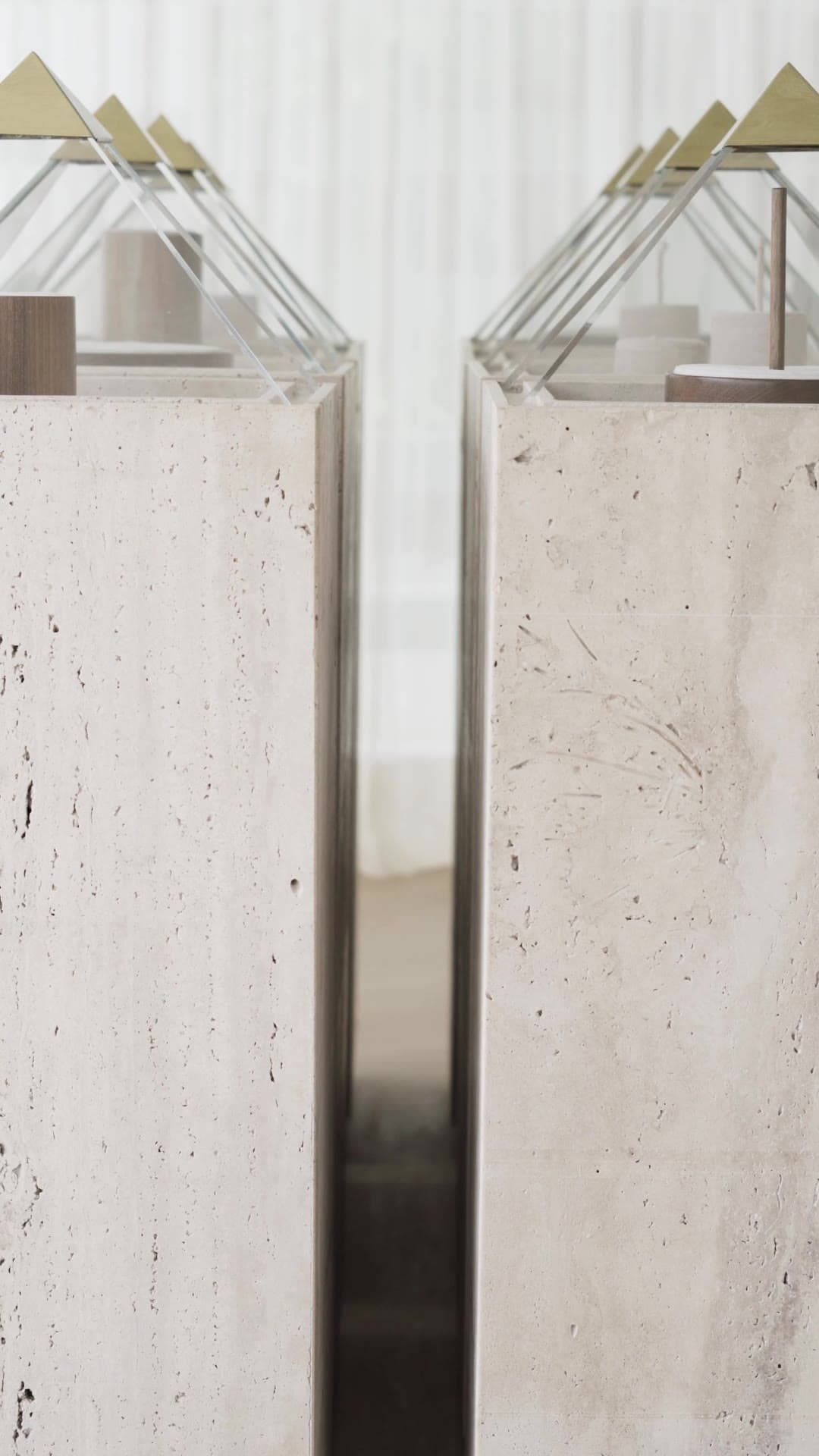 AVRA — a second vertical film: travertine plinths and glass pyramids, the walnut table and a woman reading at the green marble table.