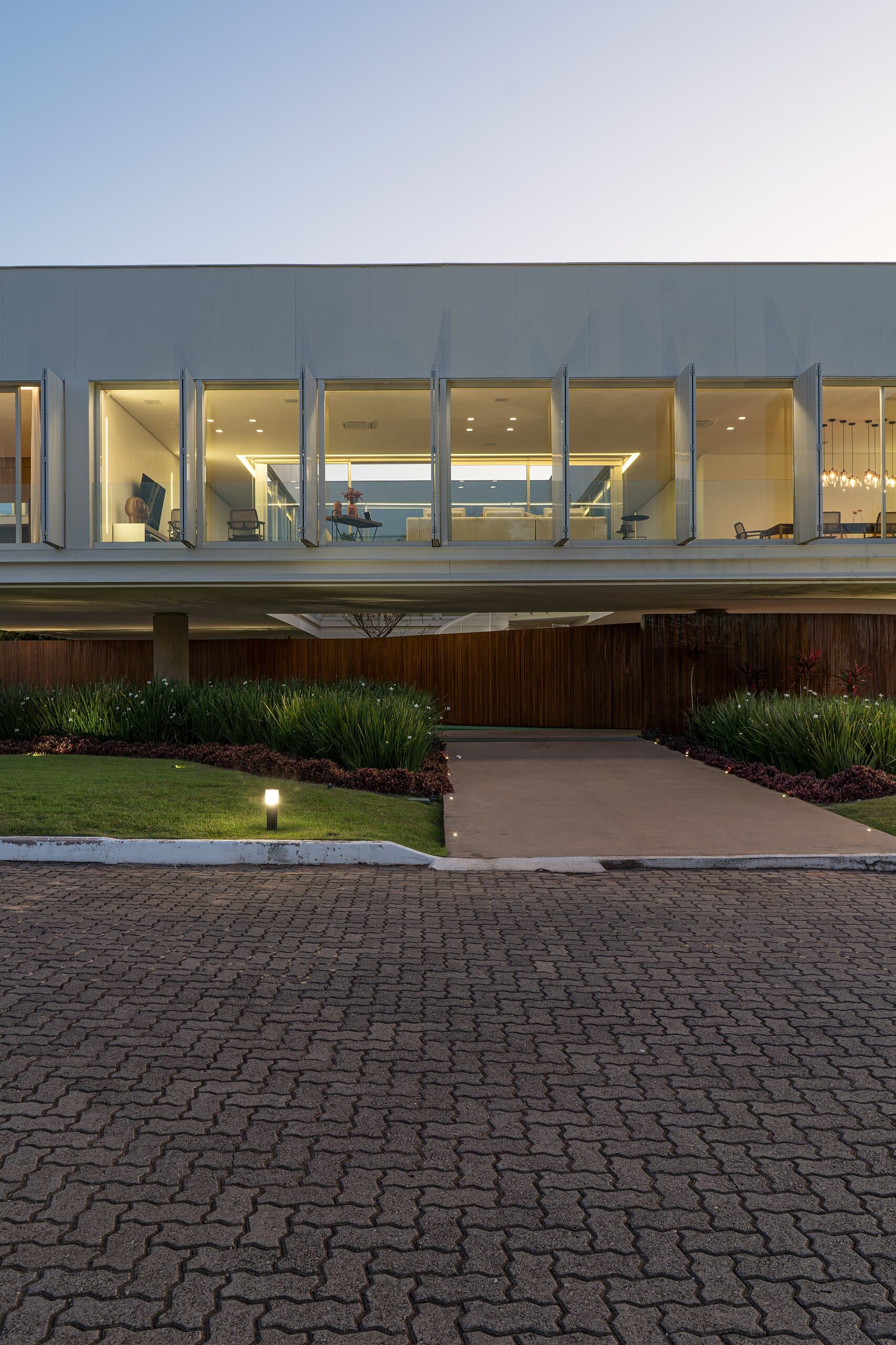 The white box at dusk, its row of windows glowing warm above the timber base.