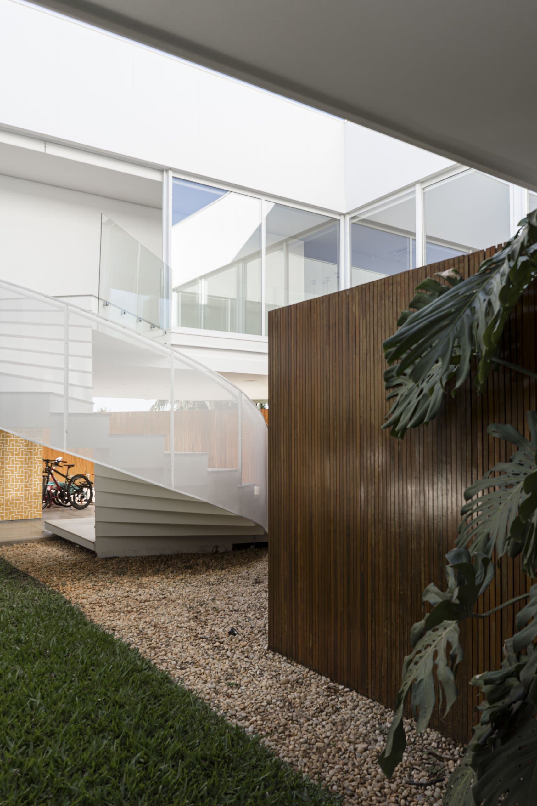 The white spiral stair behind a timber screen, monstera leaves and gravel in the foreground.