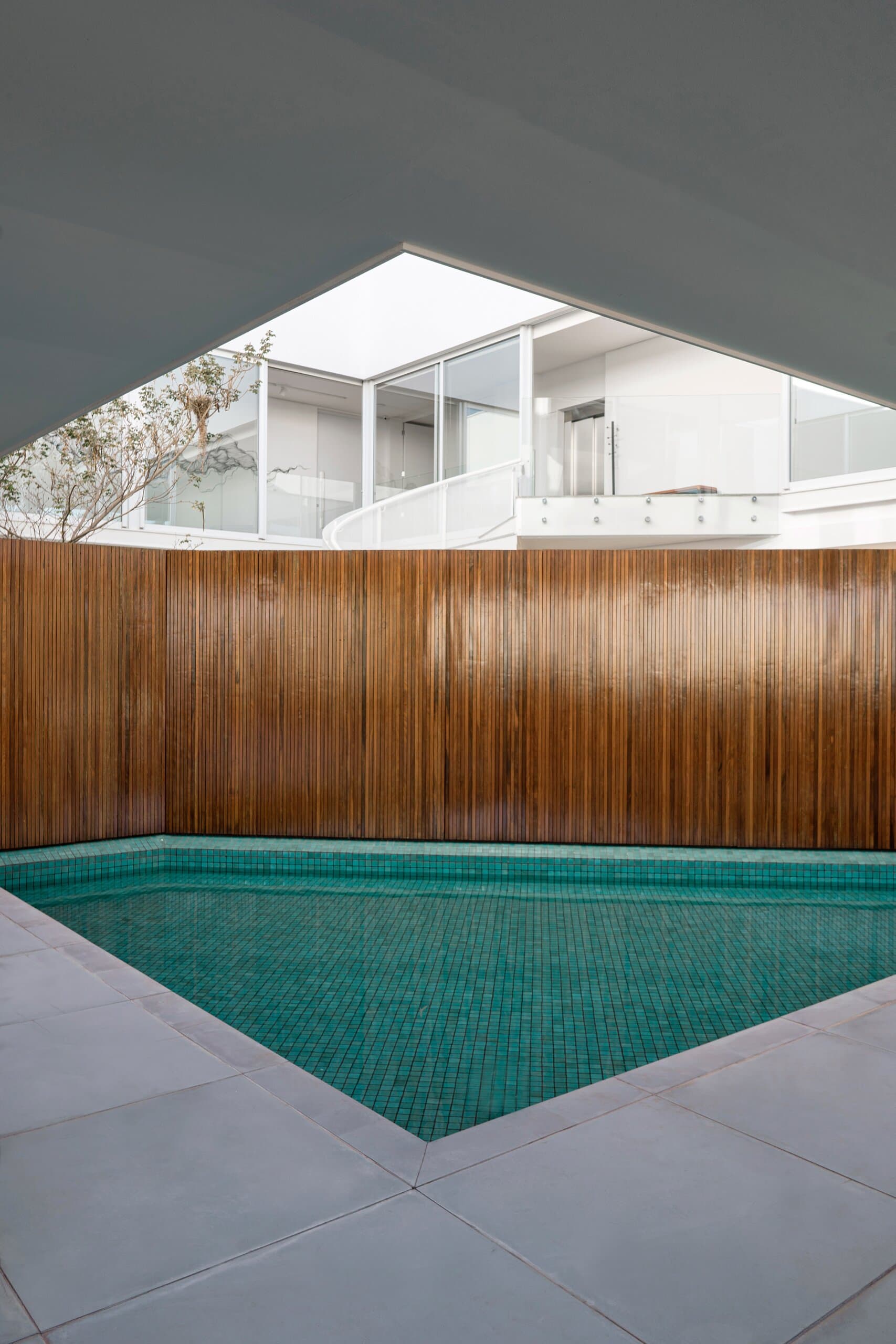A turquoise pool beneath a triangular opening in the slab, a tall timber wall behind.