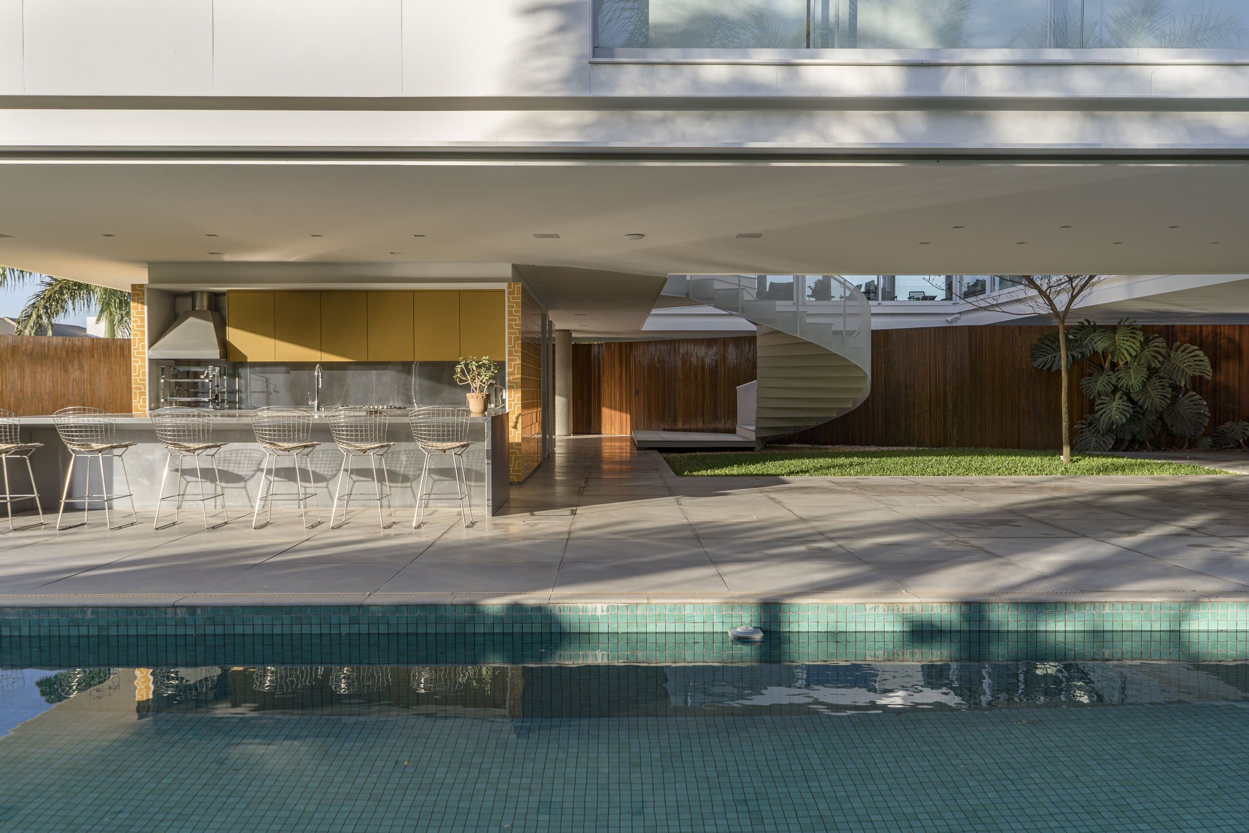 The pool reflecting an outdoor kitchen and long table under the deep white overhang.