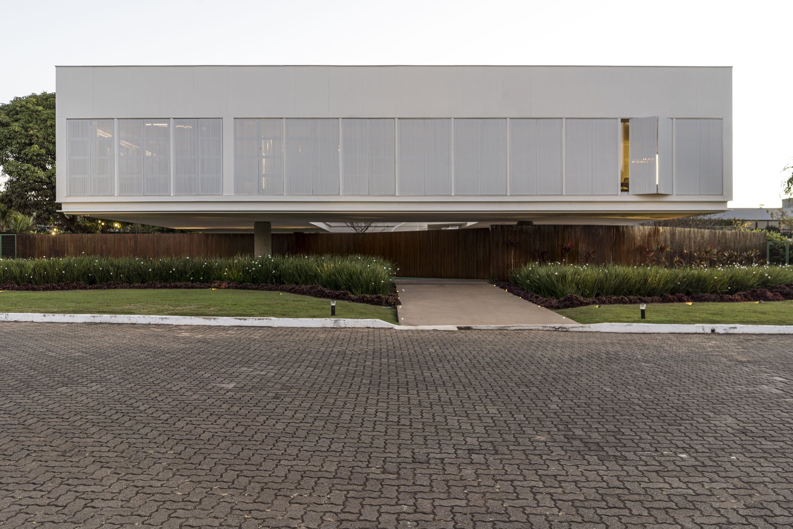 The white louvred volume hovering over a timber base and planting, brick paving in front.
