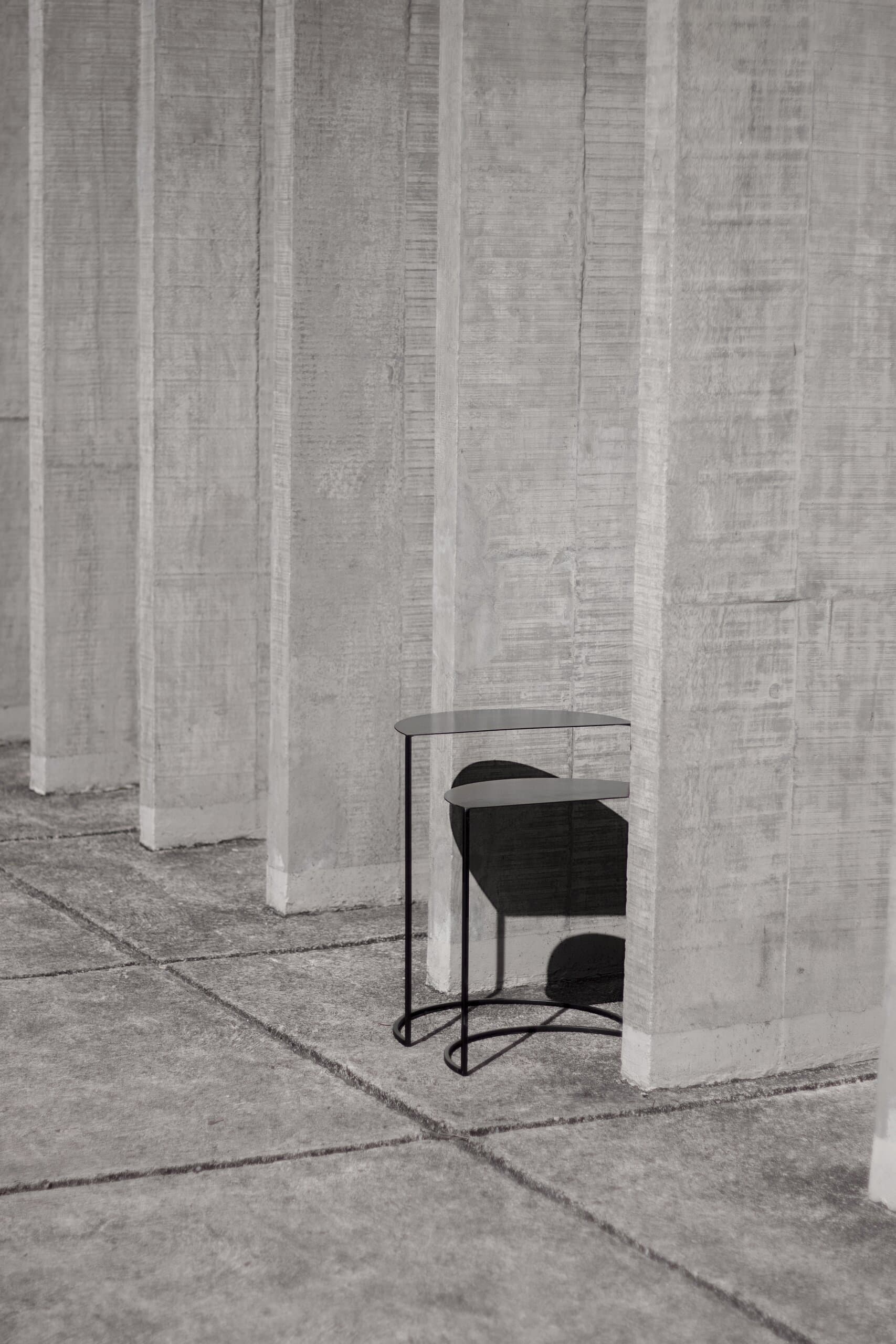A black wire chair with a half-moon seat tucked between tall concrete fins.