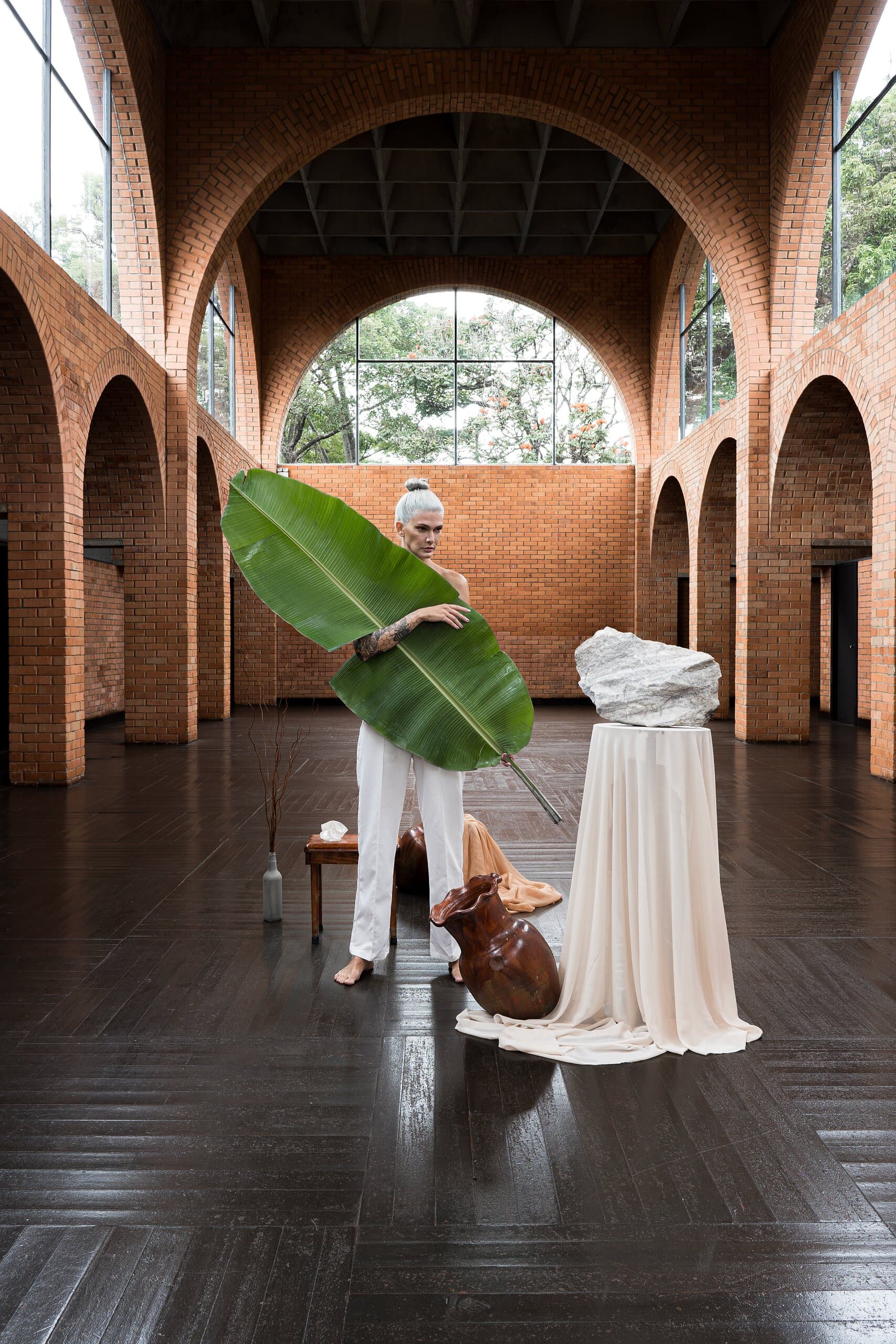 The woman in white holds a huge banana leaf beside the draped plinth in the brick arched hall.