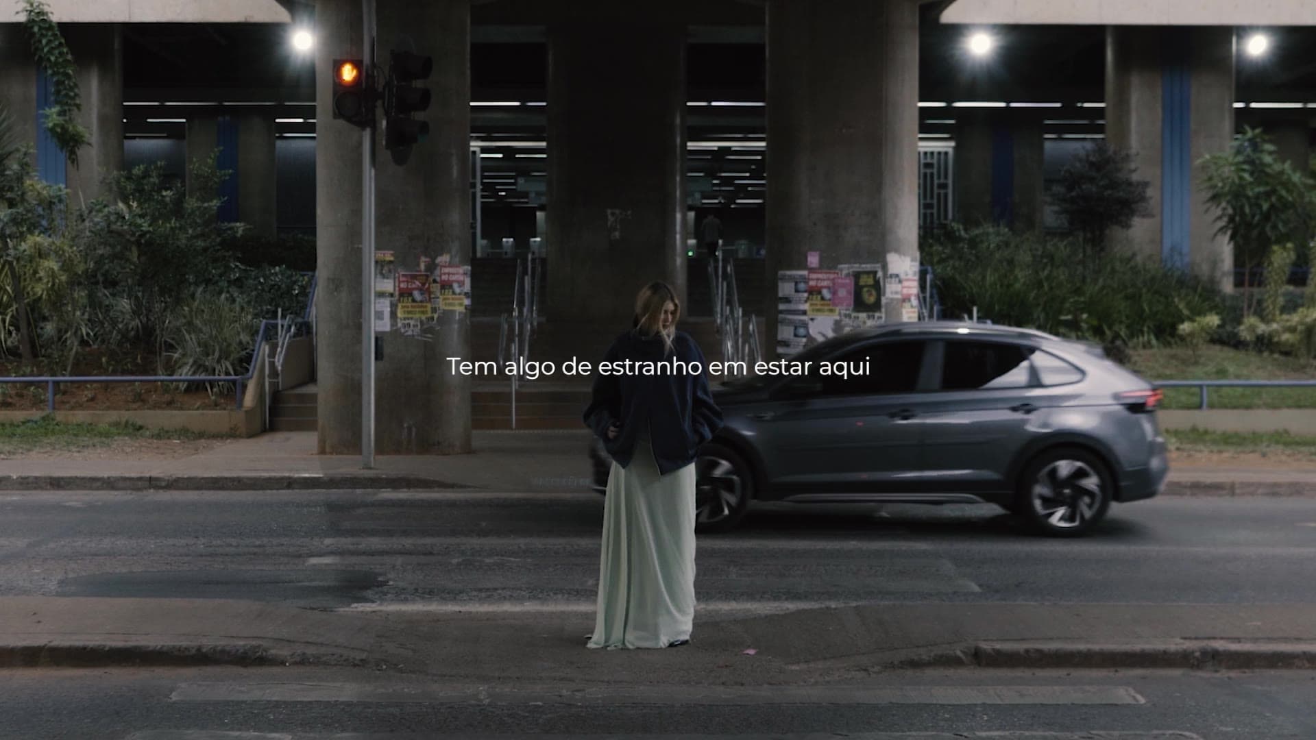 Cidade não espera — a woman stands beneath Brasília's concrete overpasses as traffic passes, with English subtitles.
