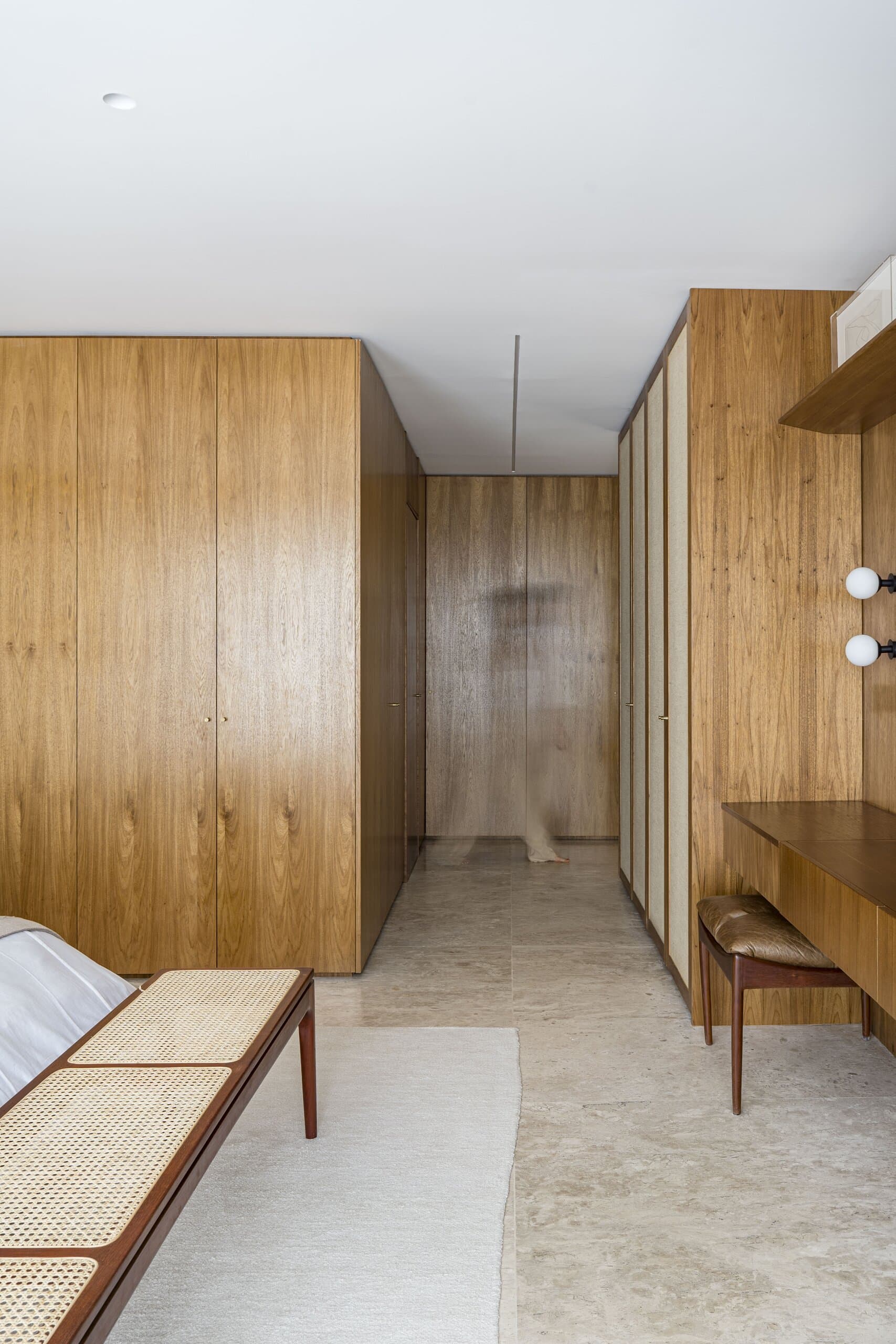 A timber-lined corridor with a pale stone floor, a cane bench and a small desk.