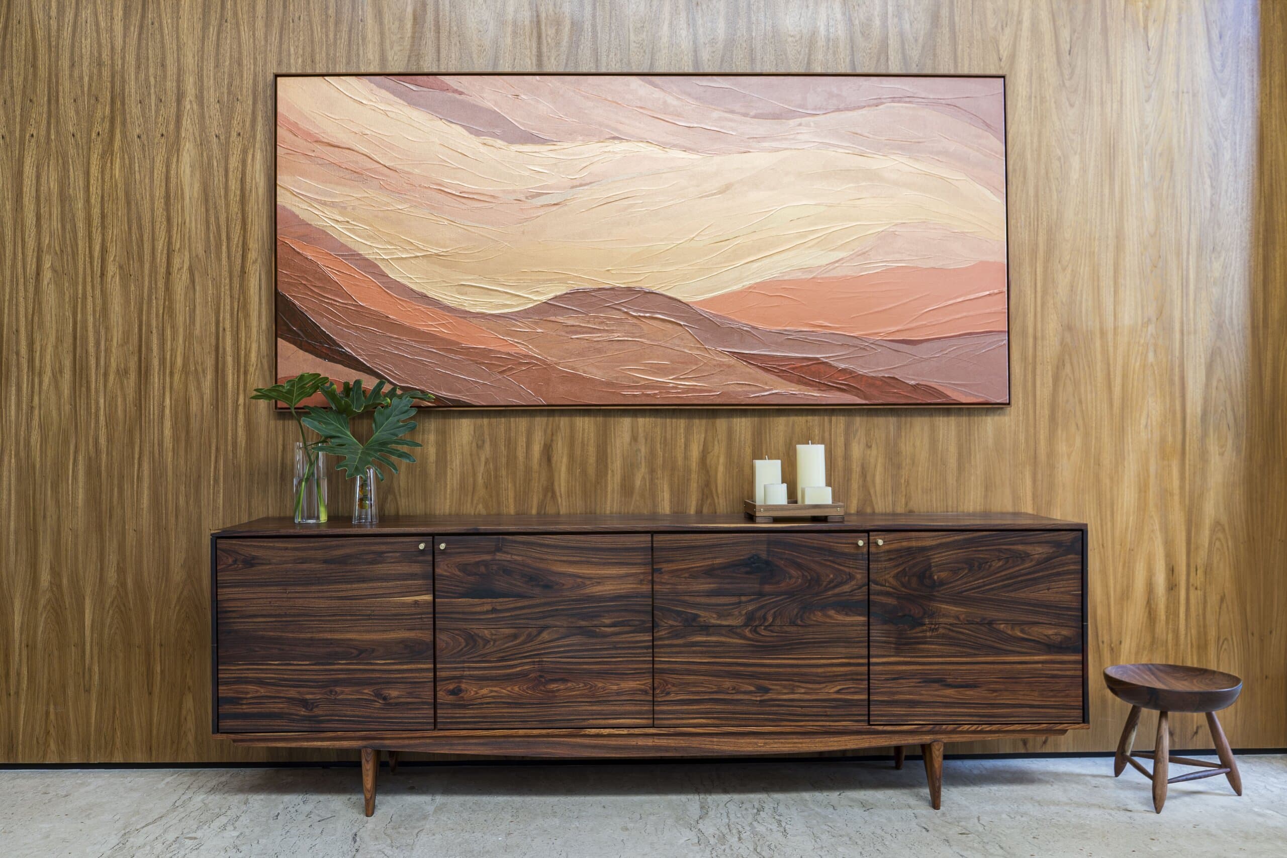 A painting of ochre landscape bands above a dark timber sideboard on a timber wall.
