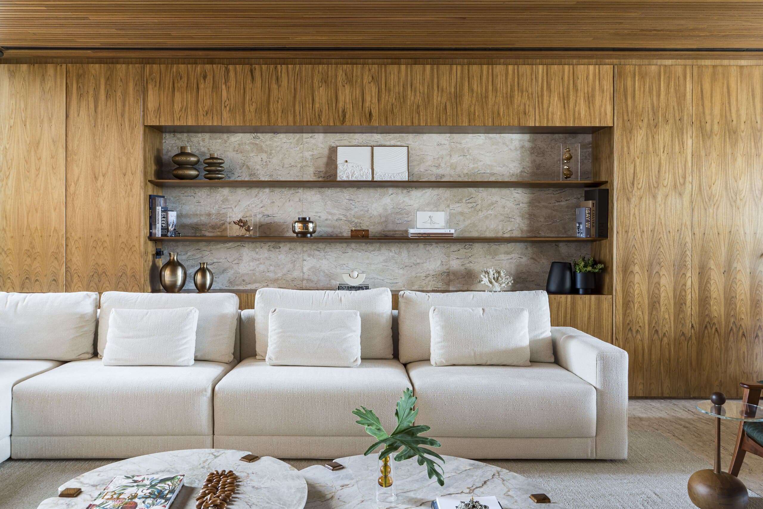 A white sofa before a timber wall with a recessed stone niche of shelves, vases and ceramics.