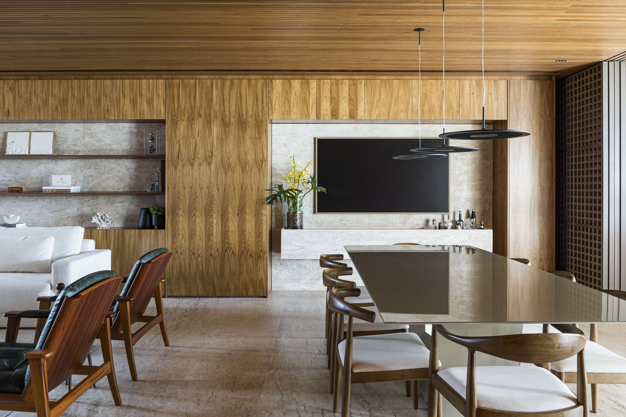 Timber chairs around a long table, the television and stone shelving set into the timber wall beyond.