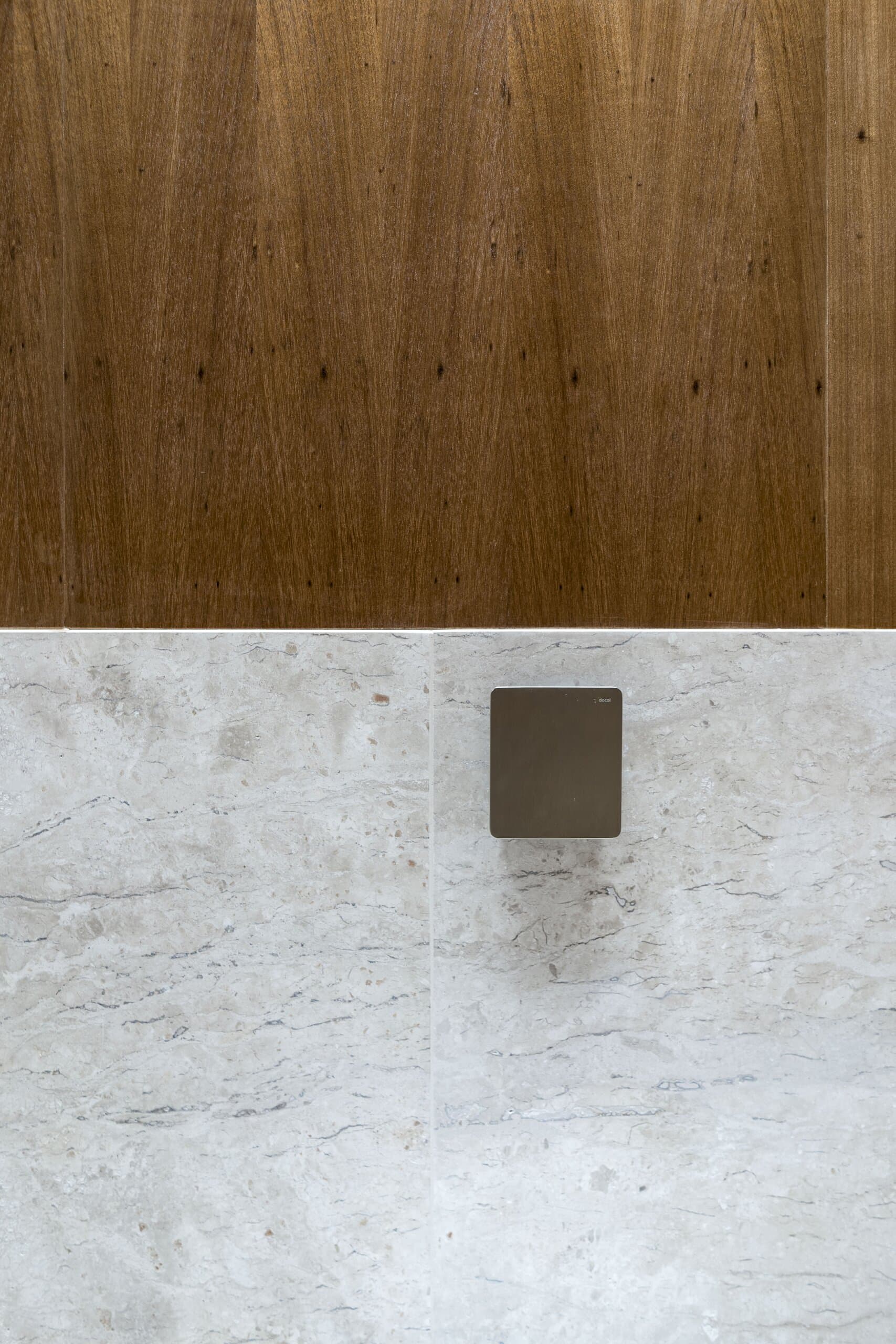 Where the timber panelling meets pale veined stone, a small bronze plate set into the wall.