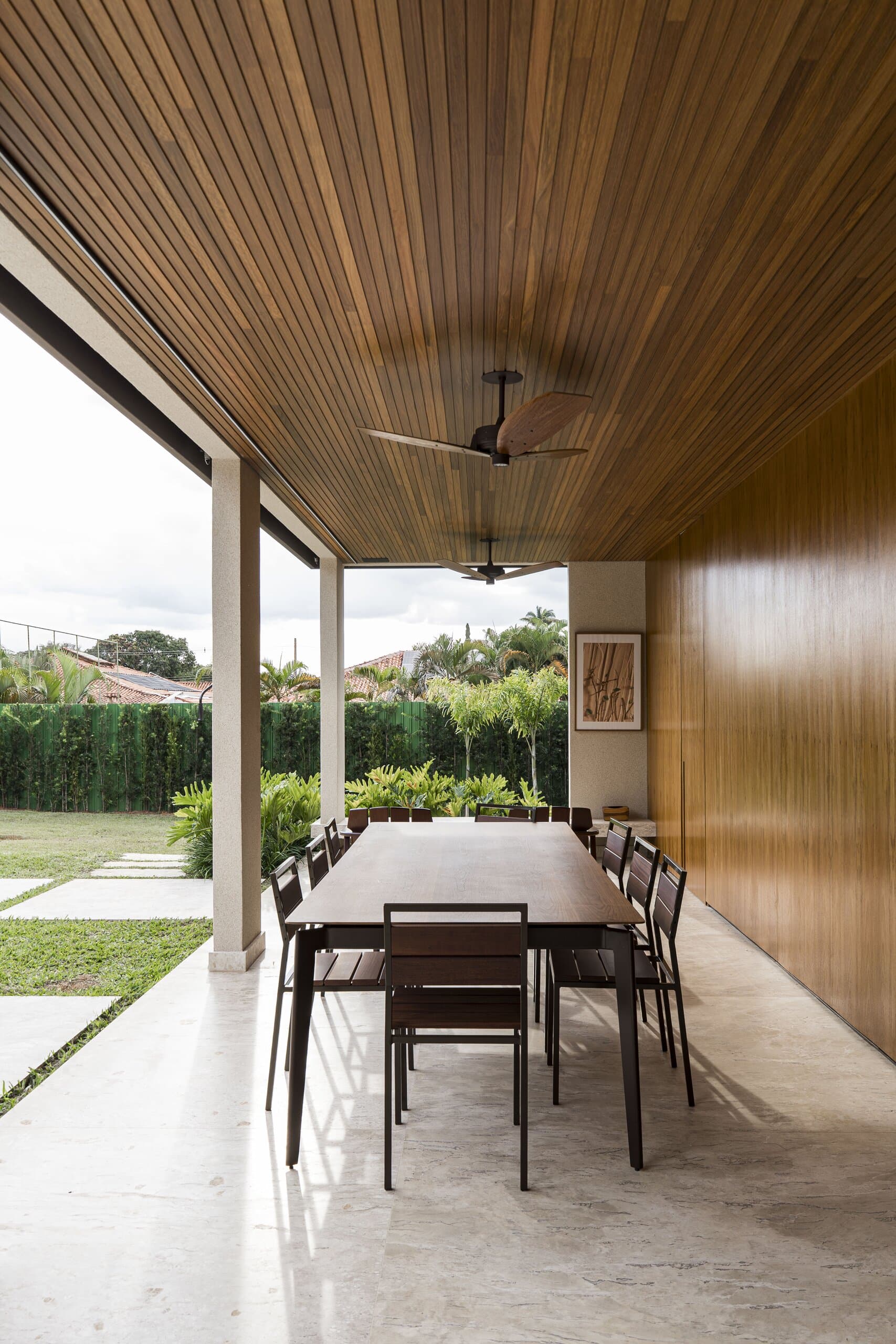 A covered terrace with a timber ceiling, a long outdoor table with black chairs and the lawn beyond.