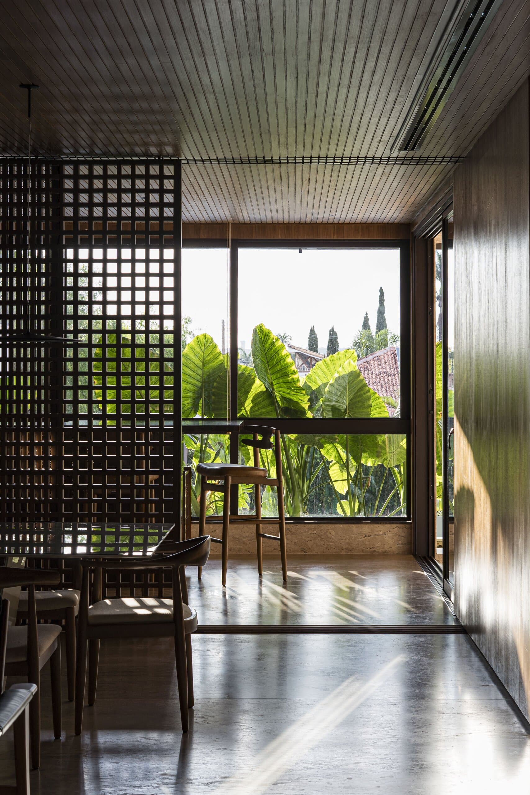 A black lattice screen and a tall window of banana leaves in a dark room with a polished floor.