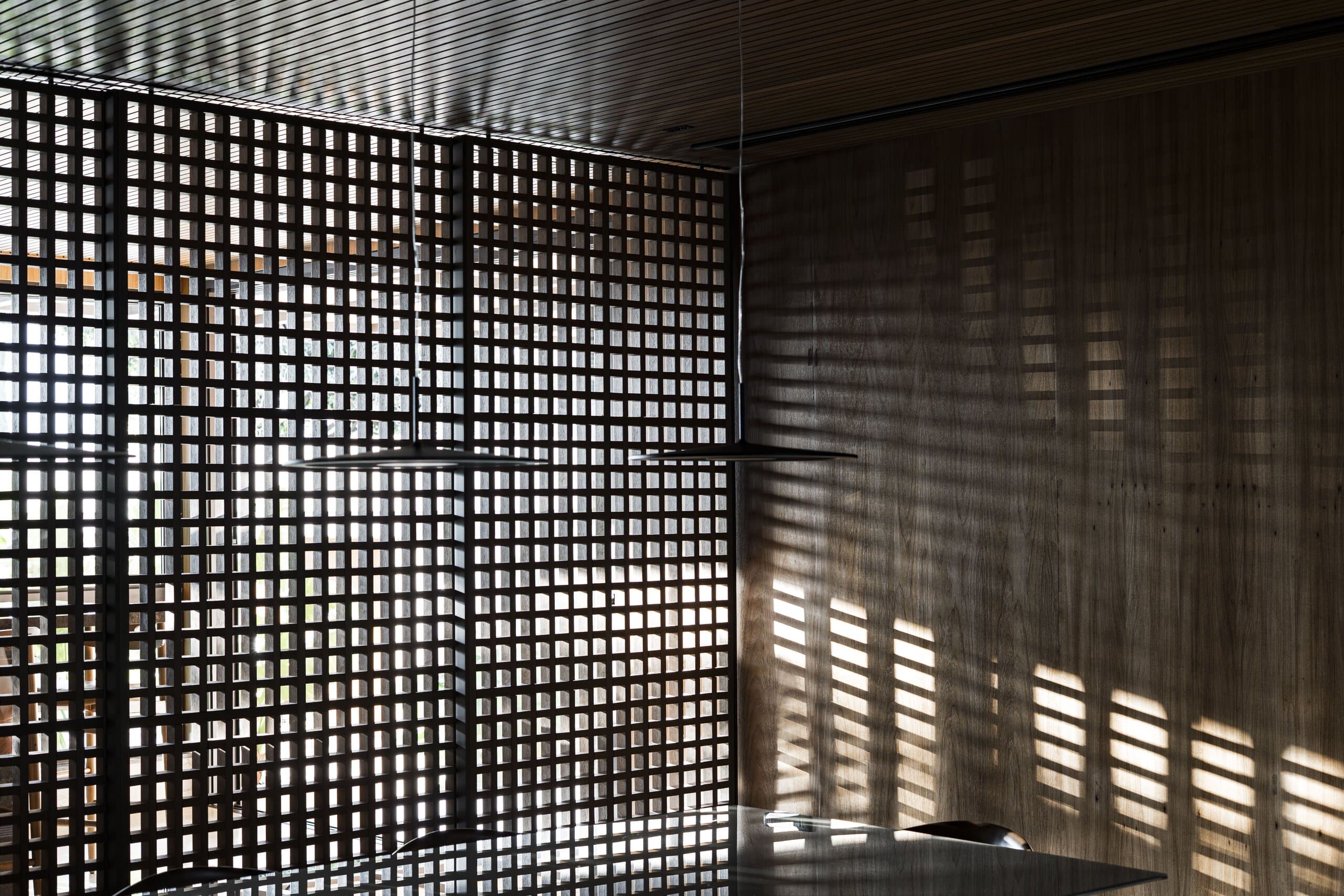 Sunlight through a dark lattice casts a grid of shadows across the wall and table.