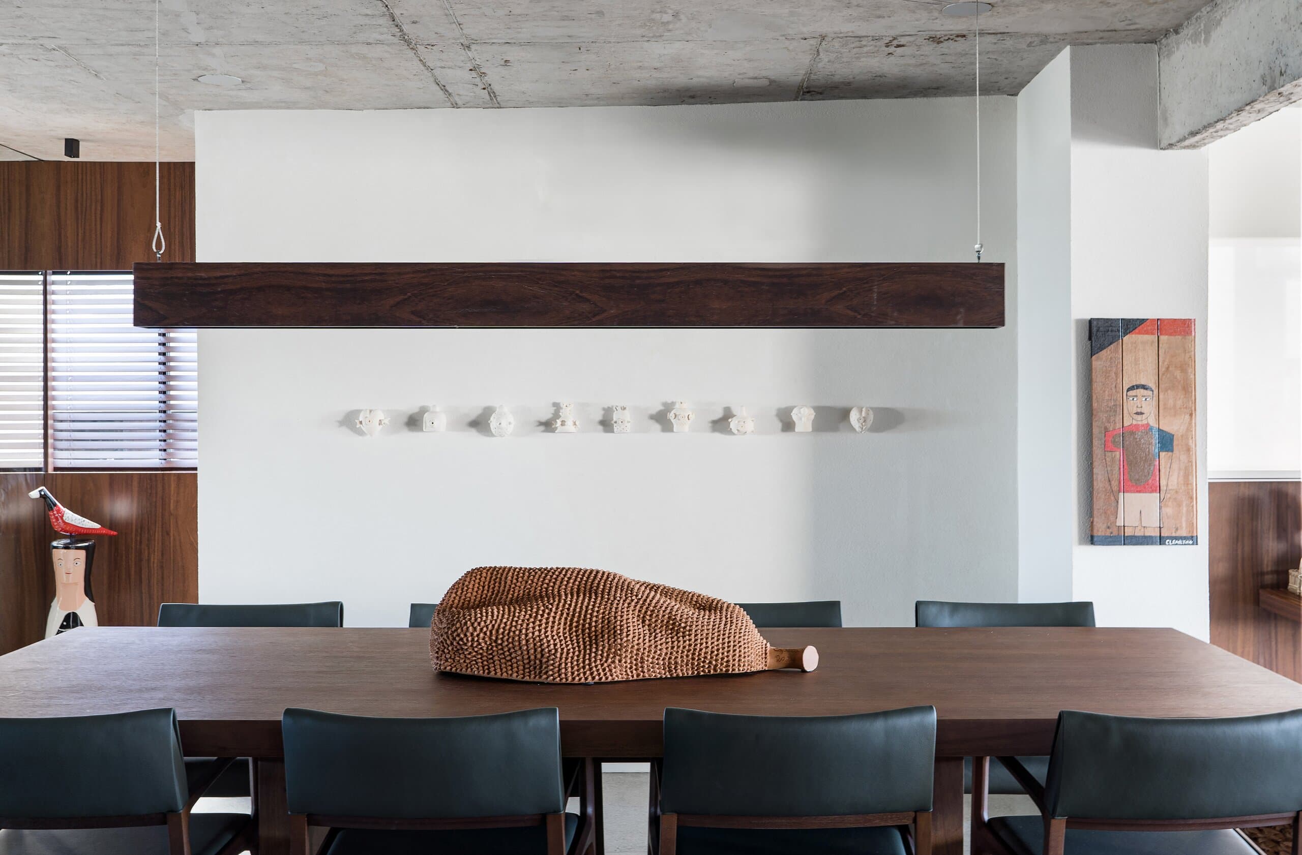 Uma mesa de jantar de madeira escura e cadeiras de couro preto sob uma viga de madeira suspensa, com pequenas cerâmicas brancas na parede.