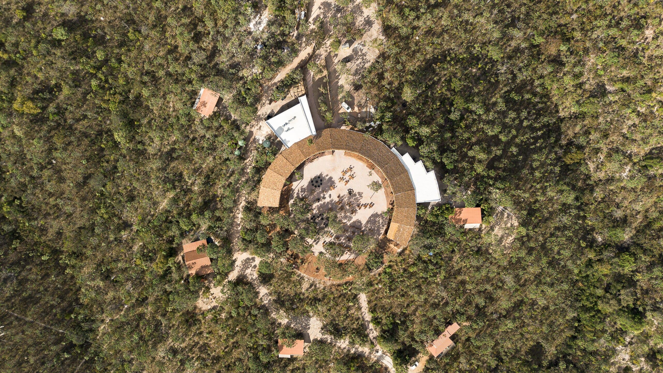 Straight down from above: the circular building, a ring in the dense green canopy, paths winding away from it.