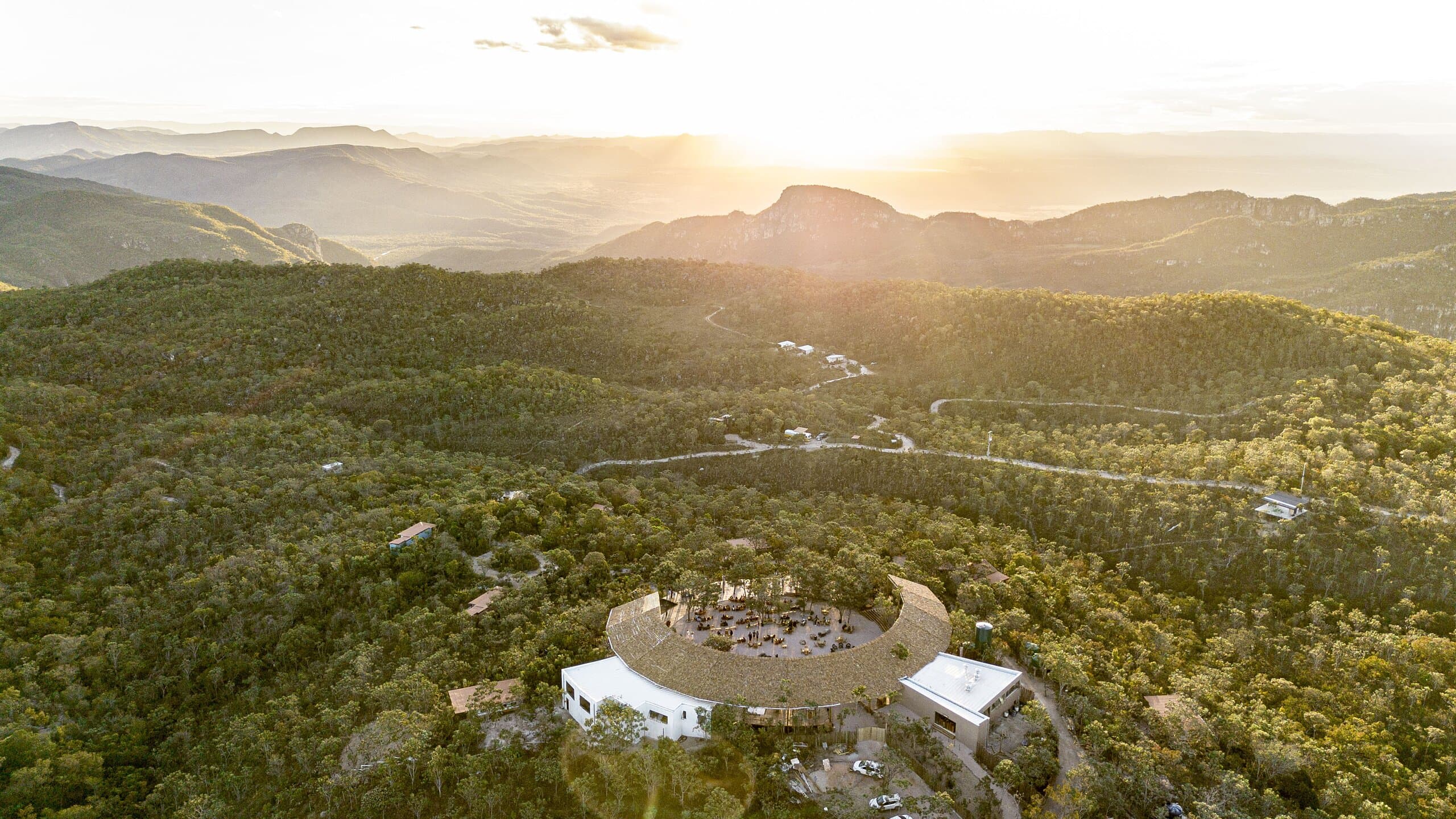 Sun setting behind a mountain peak, the round building on its hill in the forested valley below.