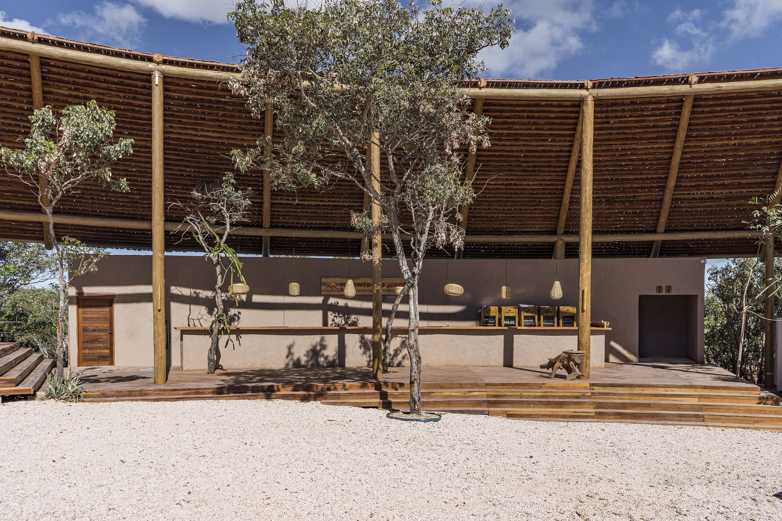 The curving thatched roof over a long bar counter, a tree rising from the white sand in front.