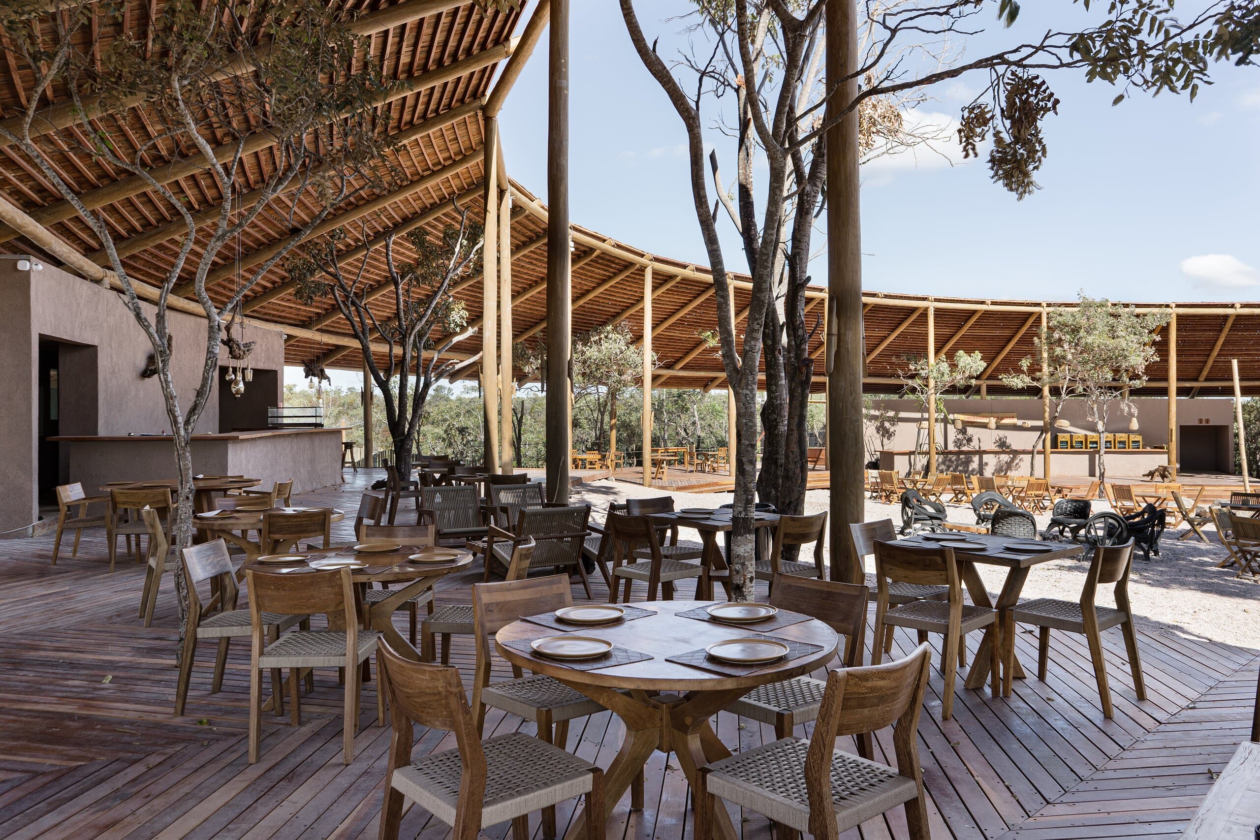 Round tables set with plates and glasses on a timber deck, the roof curving away under a blue sky.