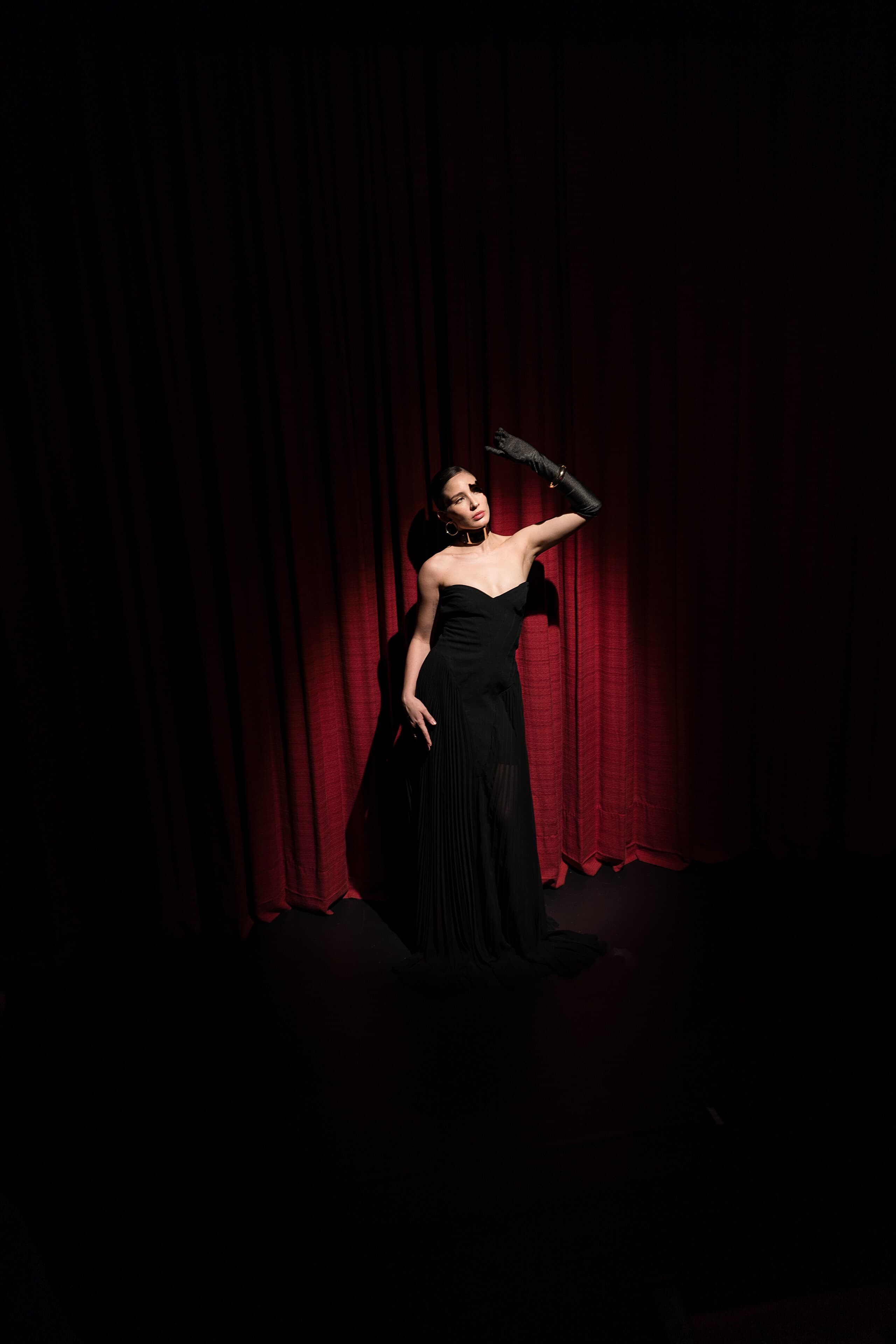 A woman in black before the red curtain, a single light from above.