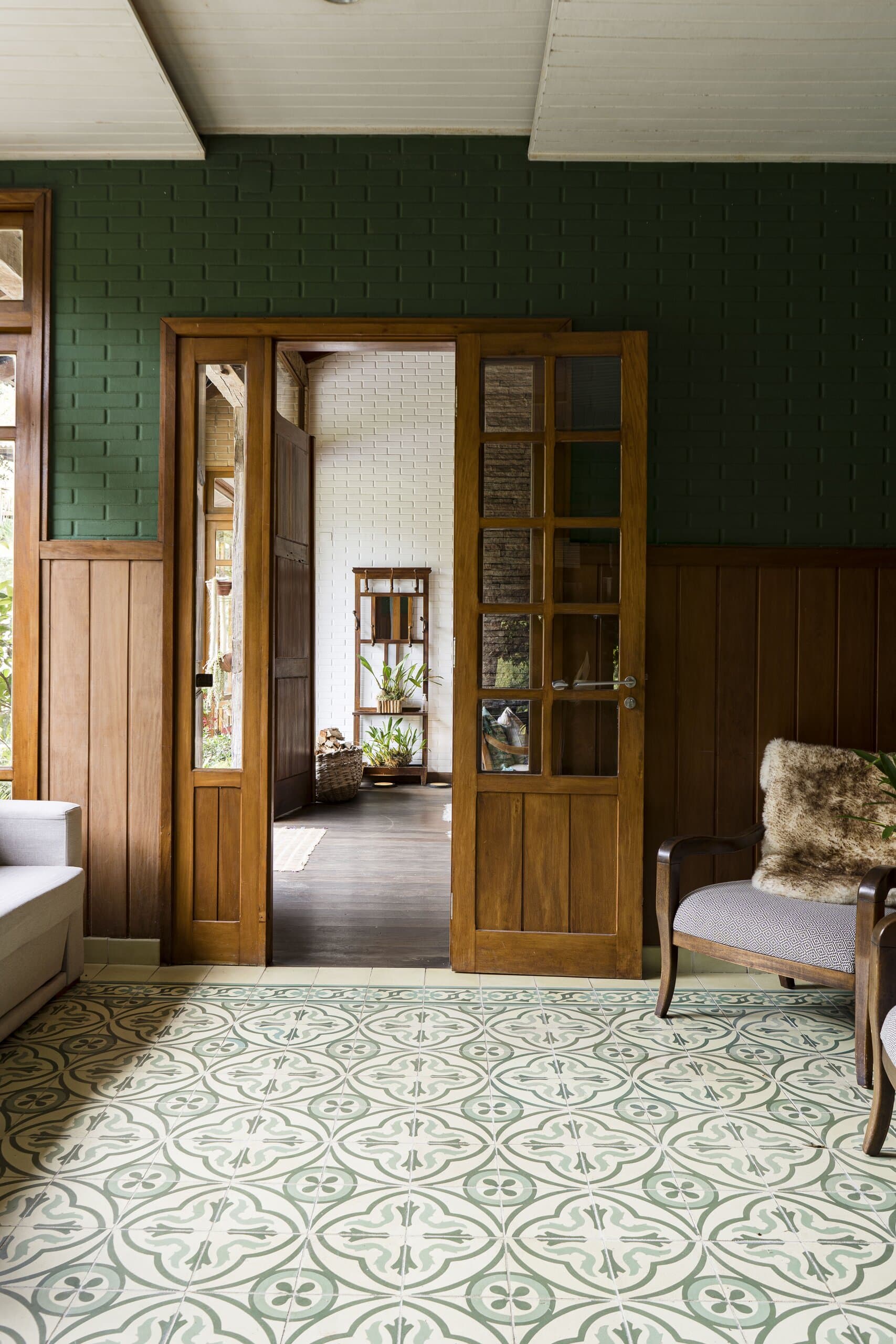 Um ambiente com paredes de azulejo verde e ladrilho hidráulico estampado, portas de madeira abertas para o cômodo seguinte.