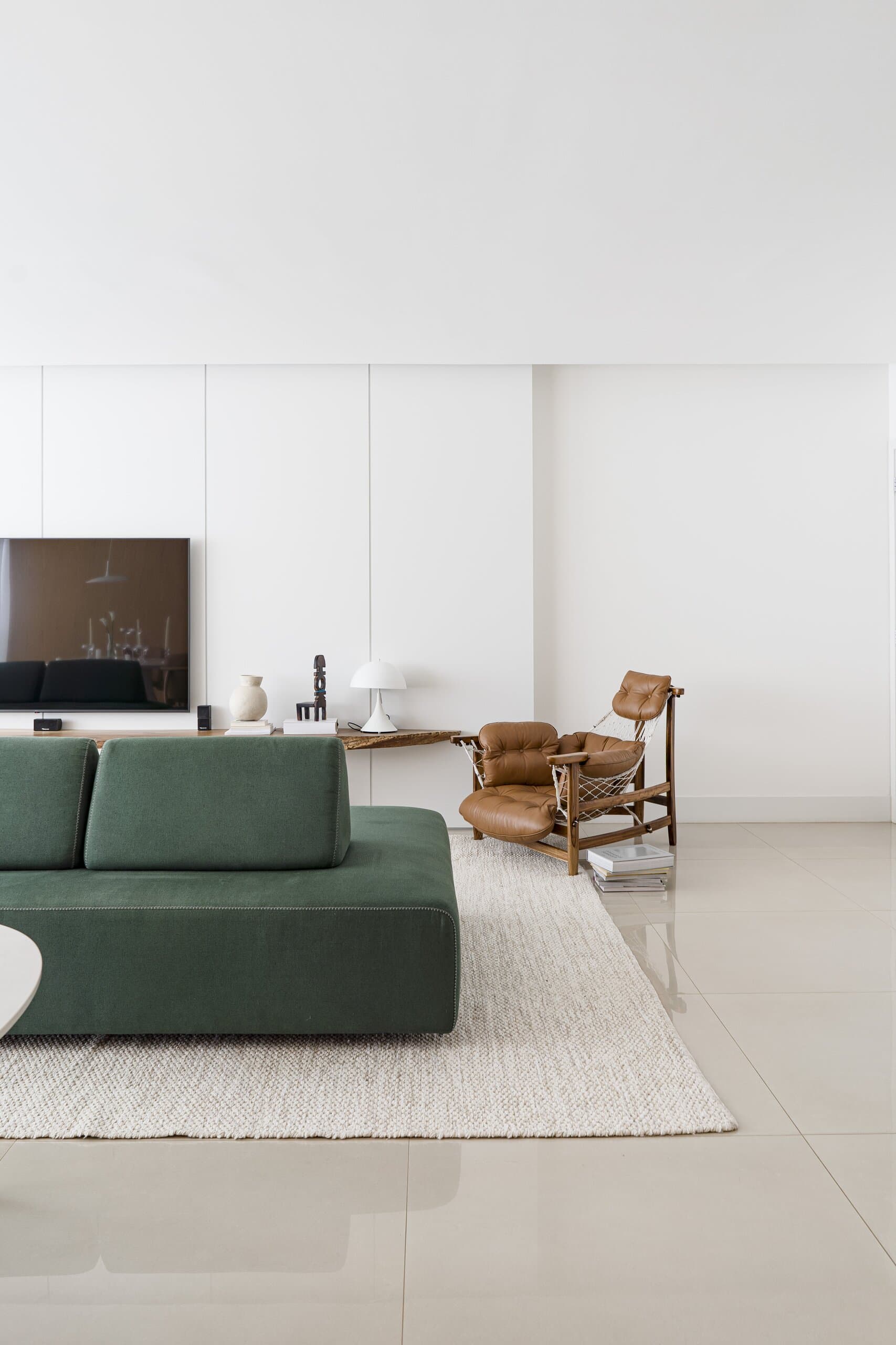 A green sofa on a pale woven rug, a leather lounge chair and a low table against a white wall of cabinets on a polished floor.