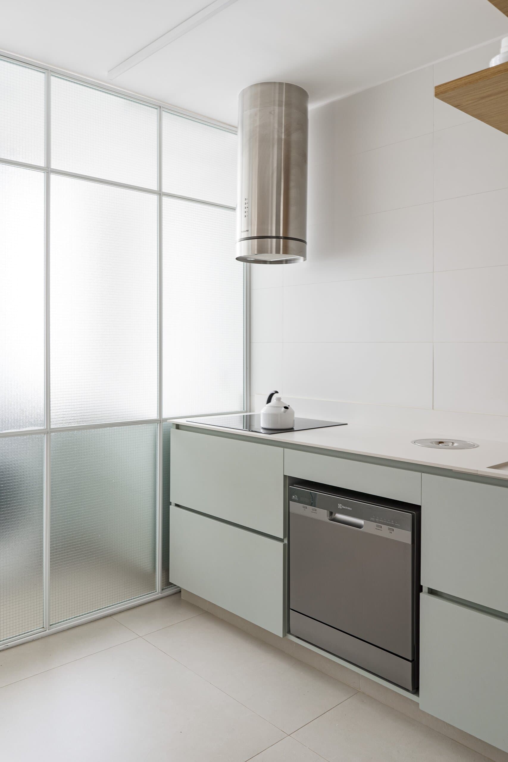 Sage-green cabinets, a steel dishwasher and a cylindrical hood beside frosted glass panels.