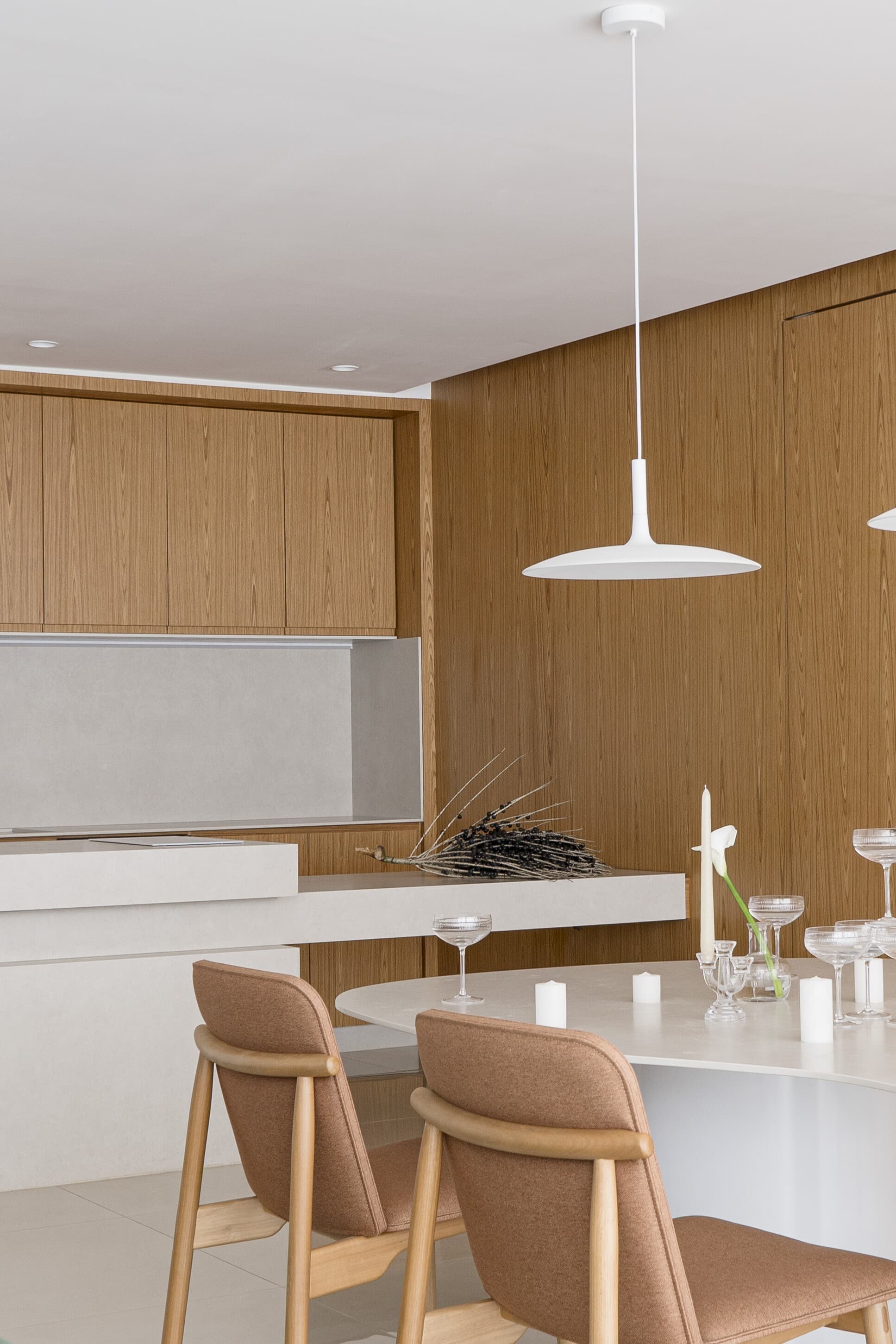 A white kitchen island with leather stools, a single pendant and a ribbed timber wall.