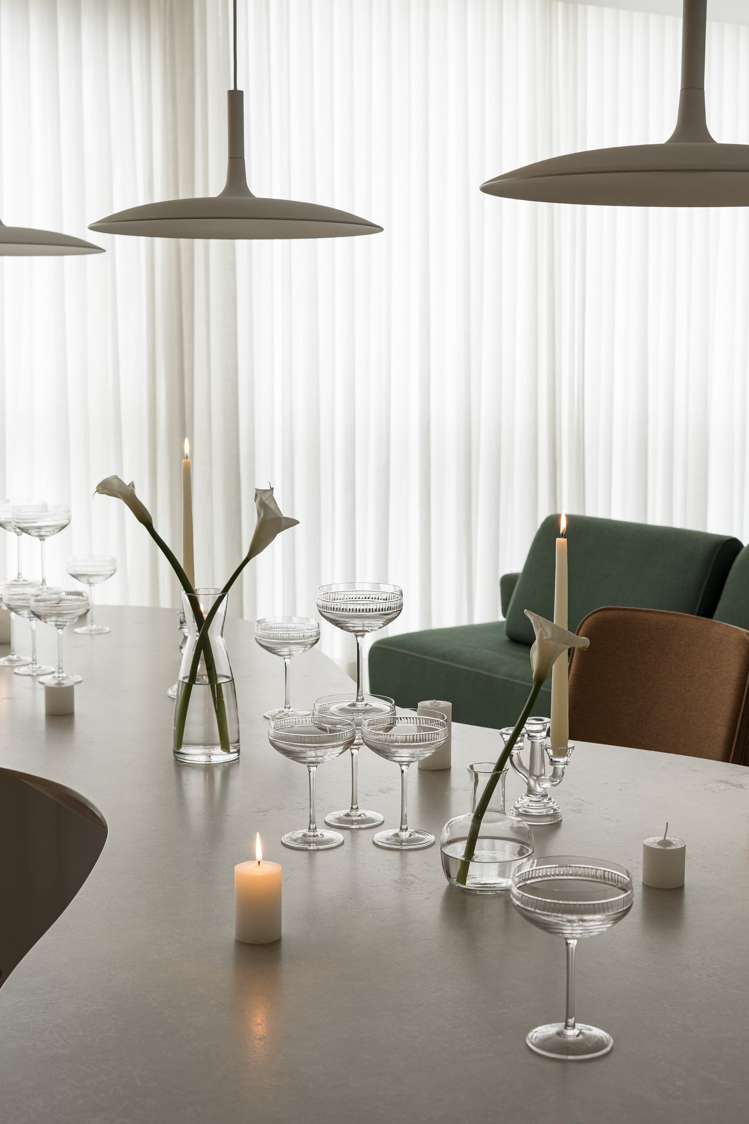 Detail: glasses, a candle and calla lilies on the table, a green armchair beyond.