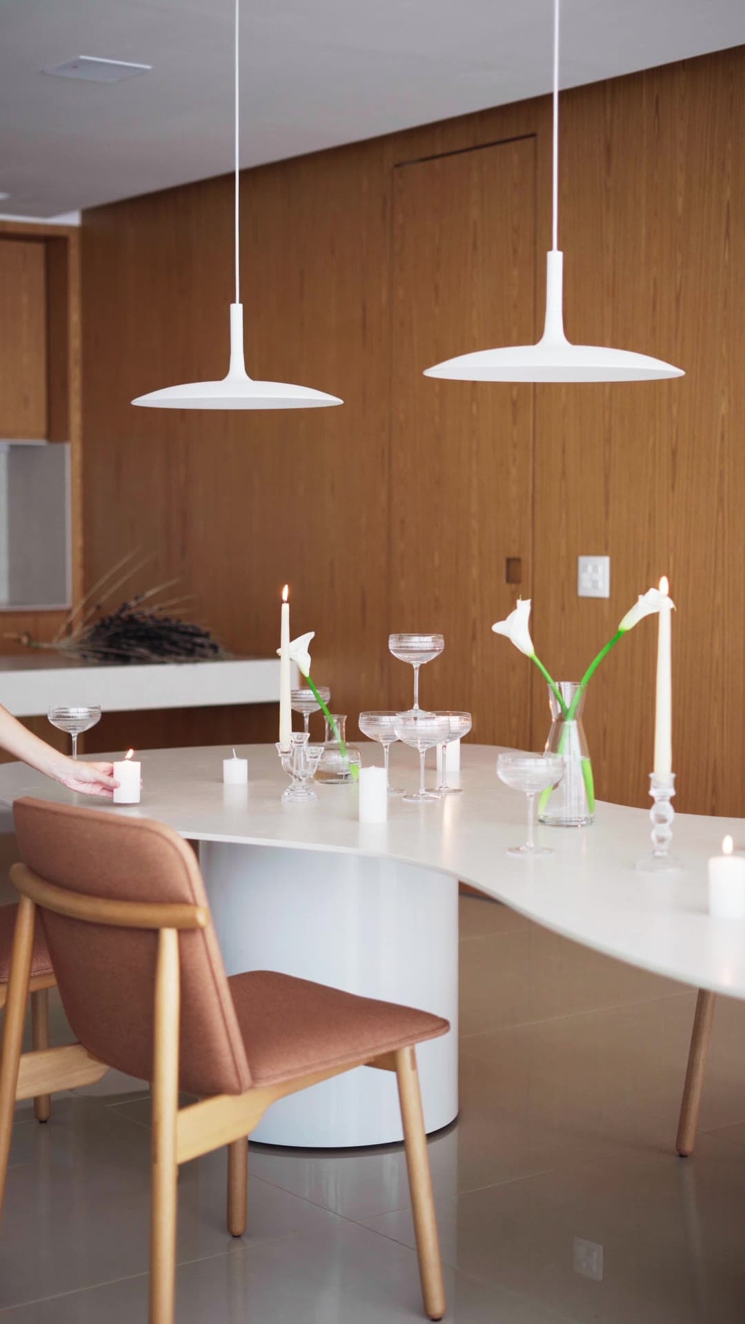 Patropi — a vertical film: the dining table and green sofa, clay pots on the rug, a woman reading and candles among glasses and calla lilies.