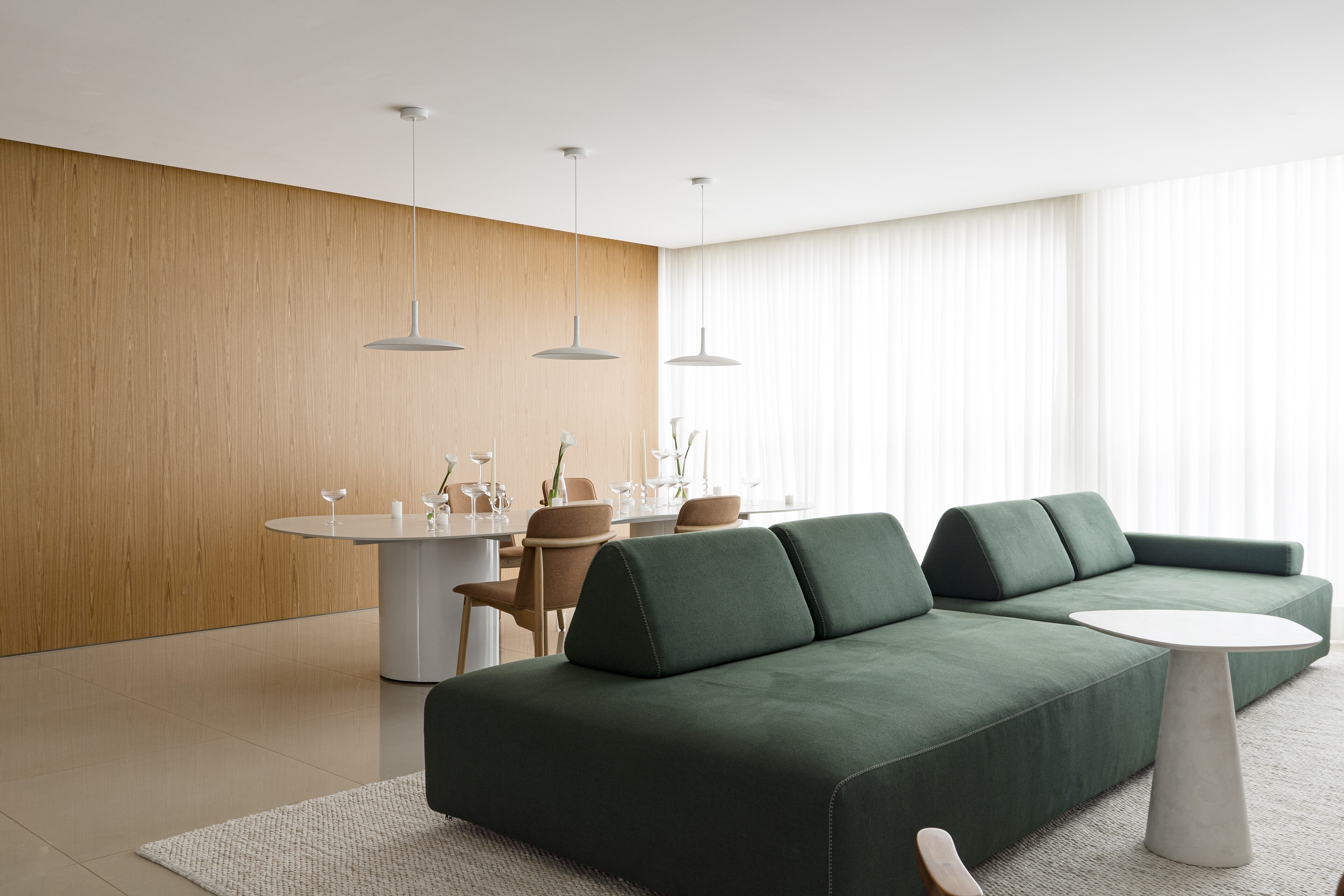 A calm living room: a deep green modular sofa, a ribbed timber wall, white pendants and sheer curtains.