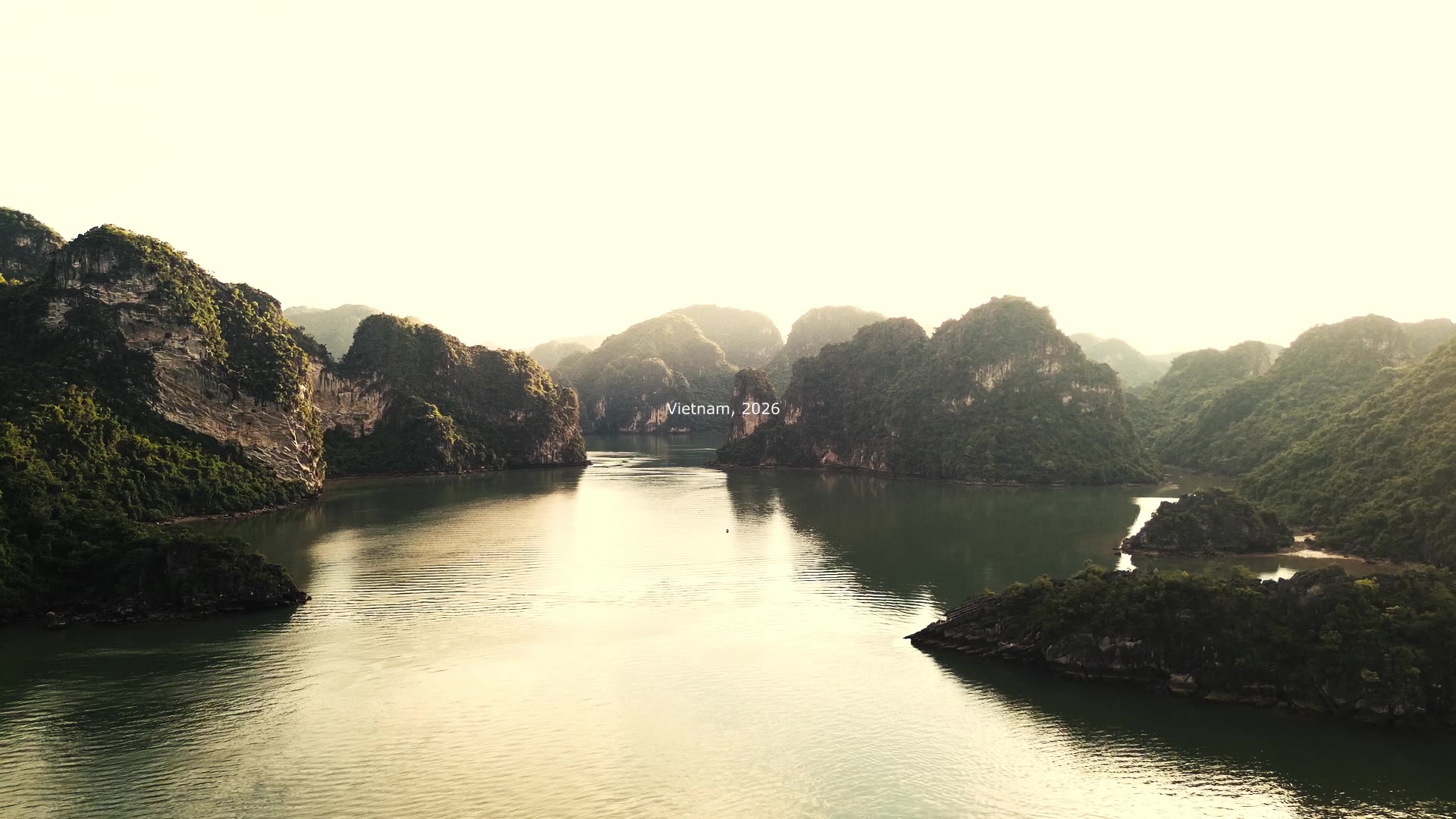 Limestone islands rise from calm green water under a hazy, pale sky.