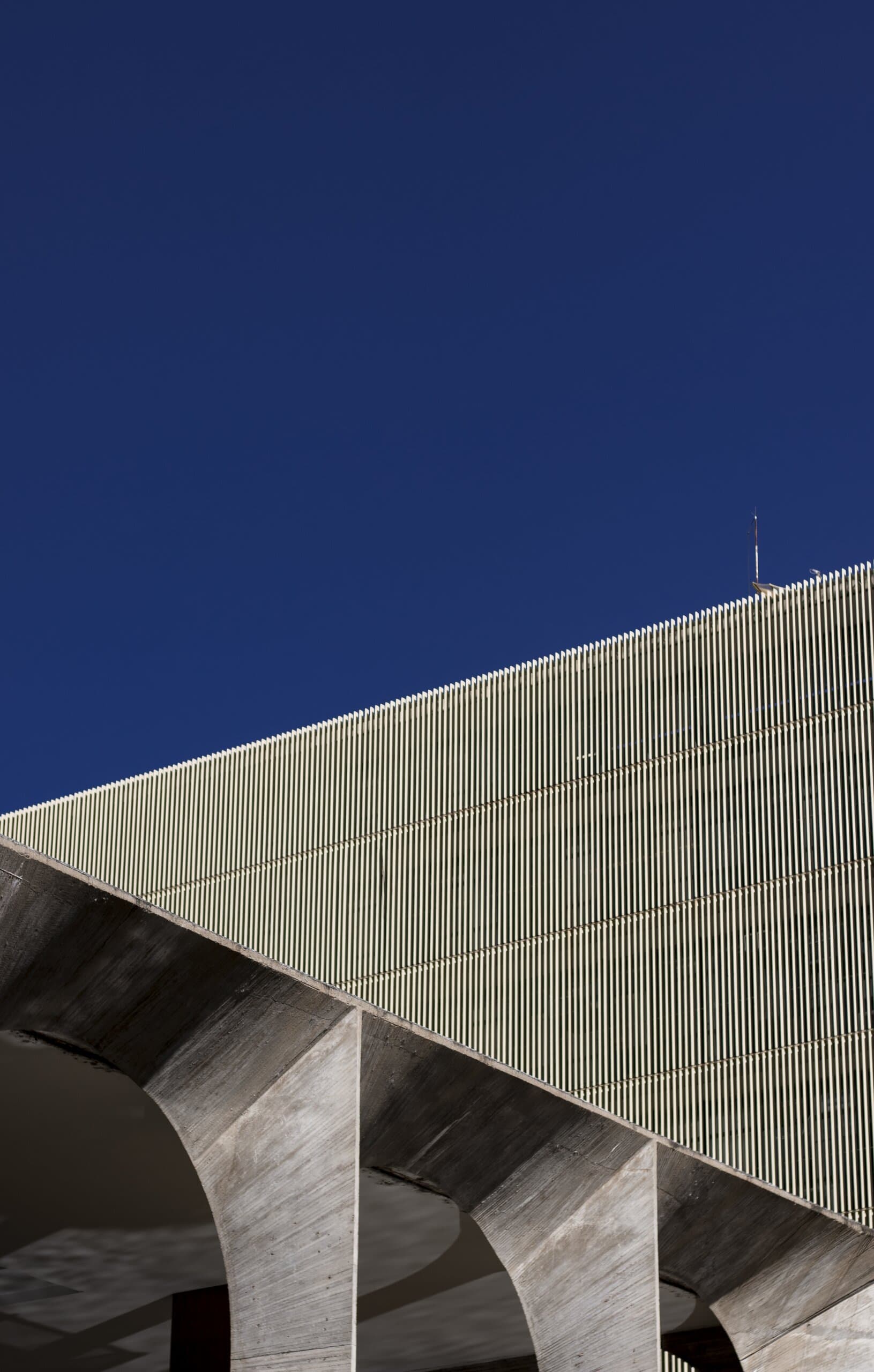 Brasília: the ribbed concrete curve of a modernist building and its arched supports against a deep blue sky.