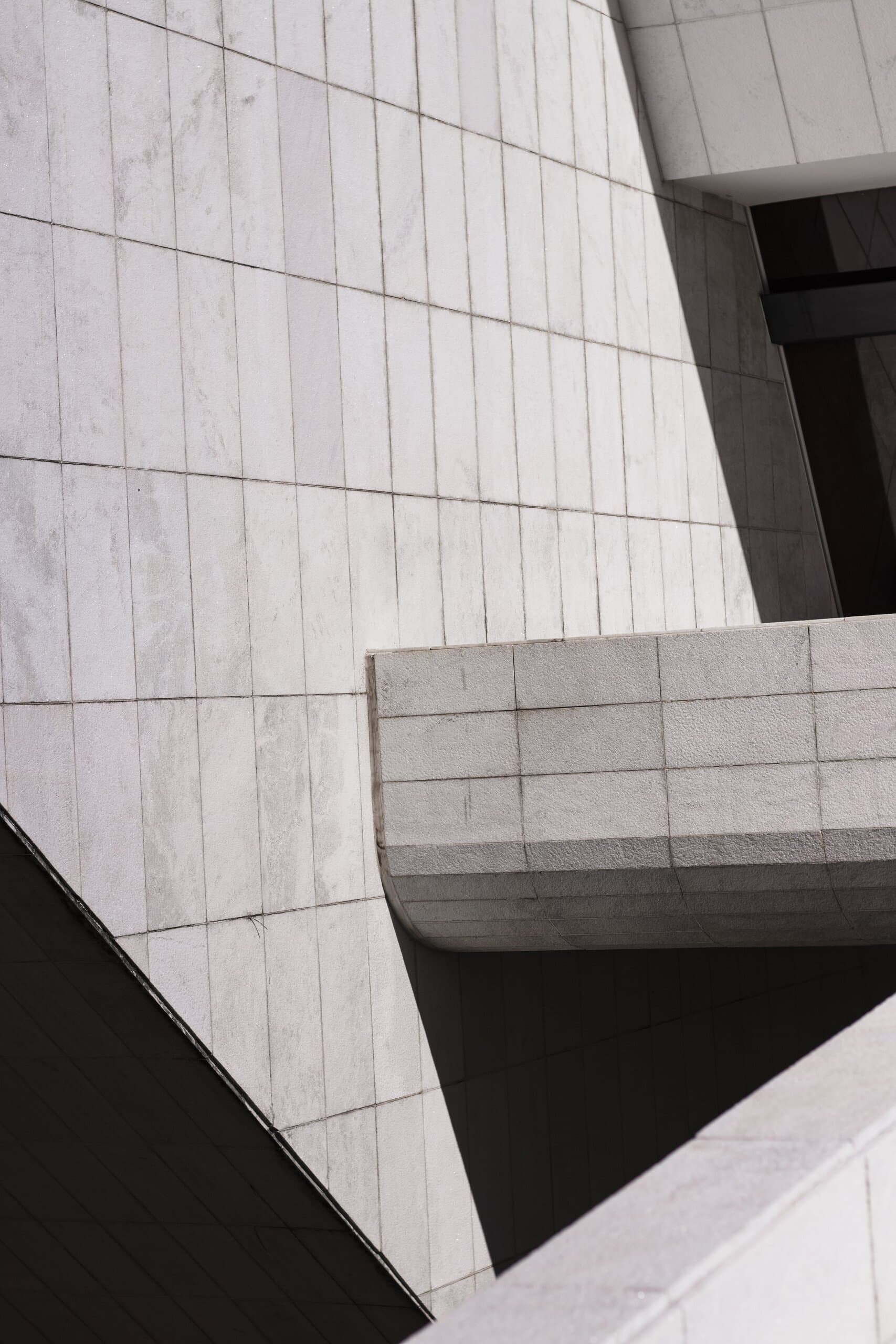 Pale stone cladding and a cantilevered concrete volume, cut by a hard diagonal shadow.