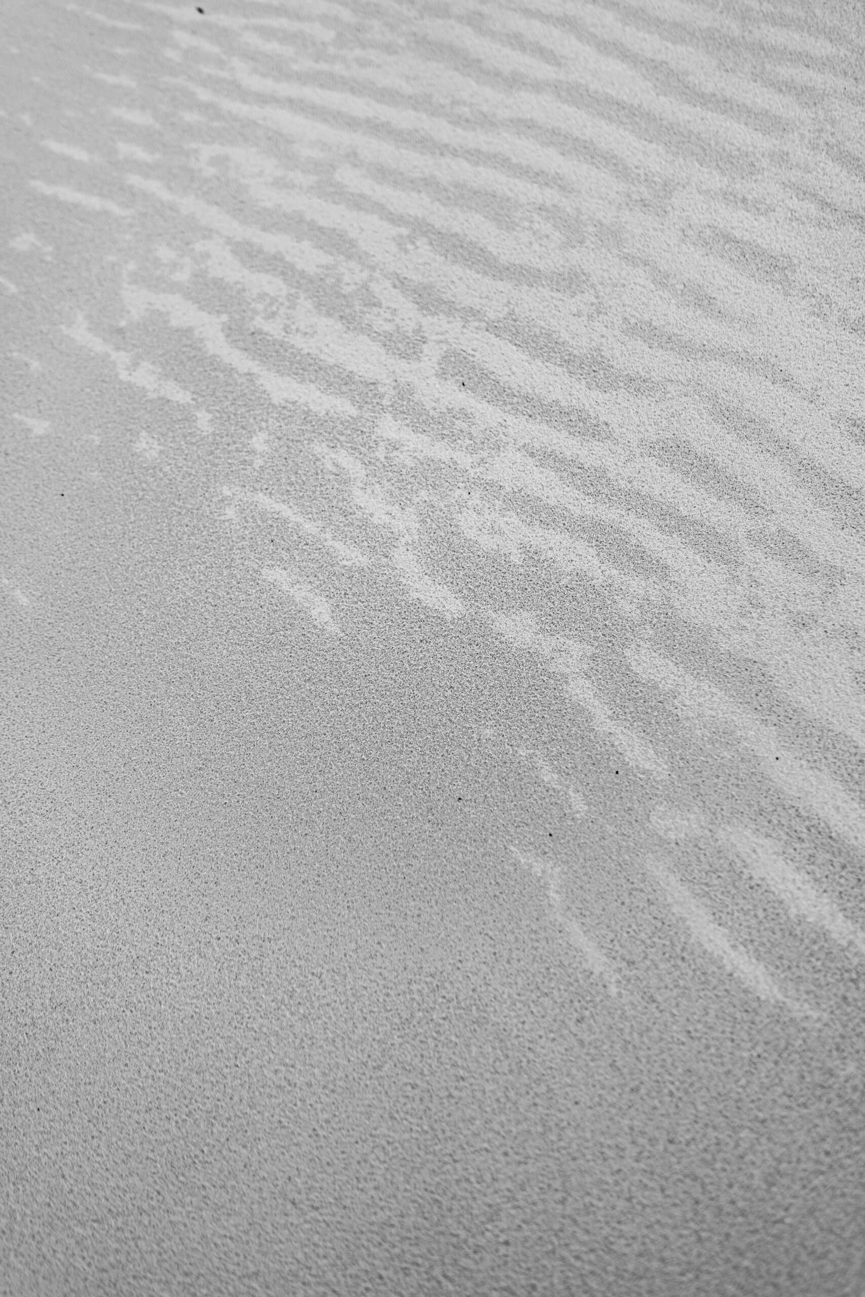 Fine ripples drawn in pale sand by water, close up.