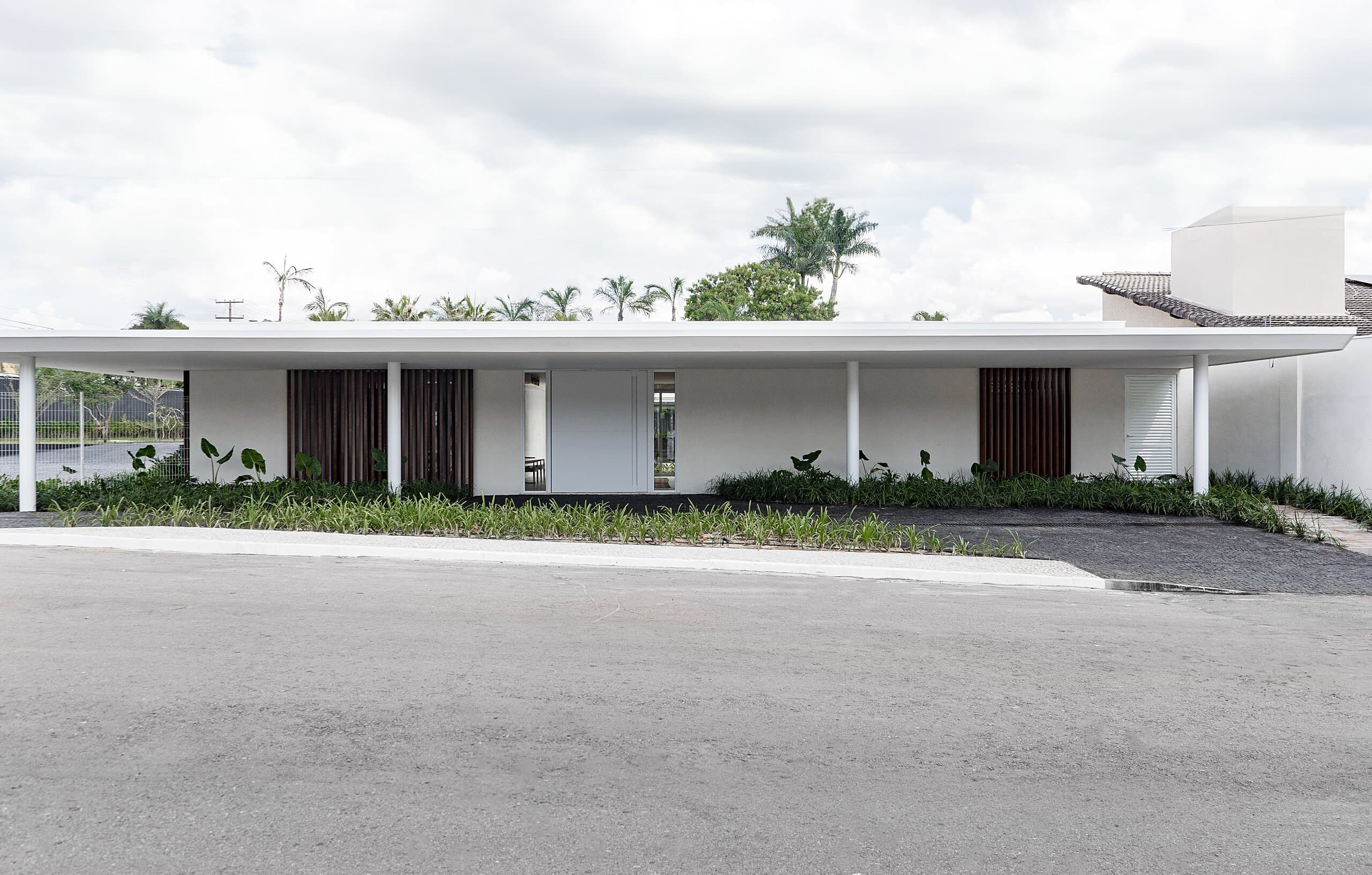 The street front: a low white building under a long flat roof, timber-slatted panels and a broad tarmac forecourt.