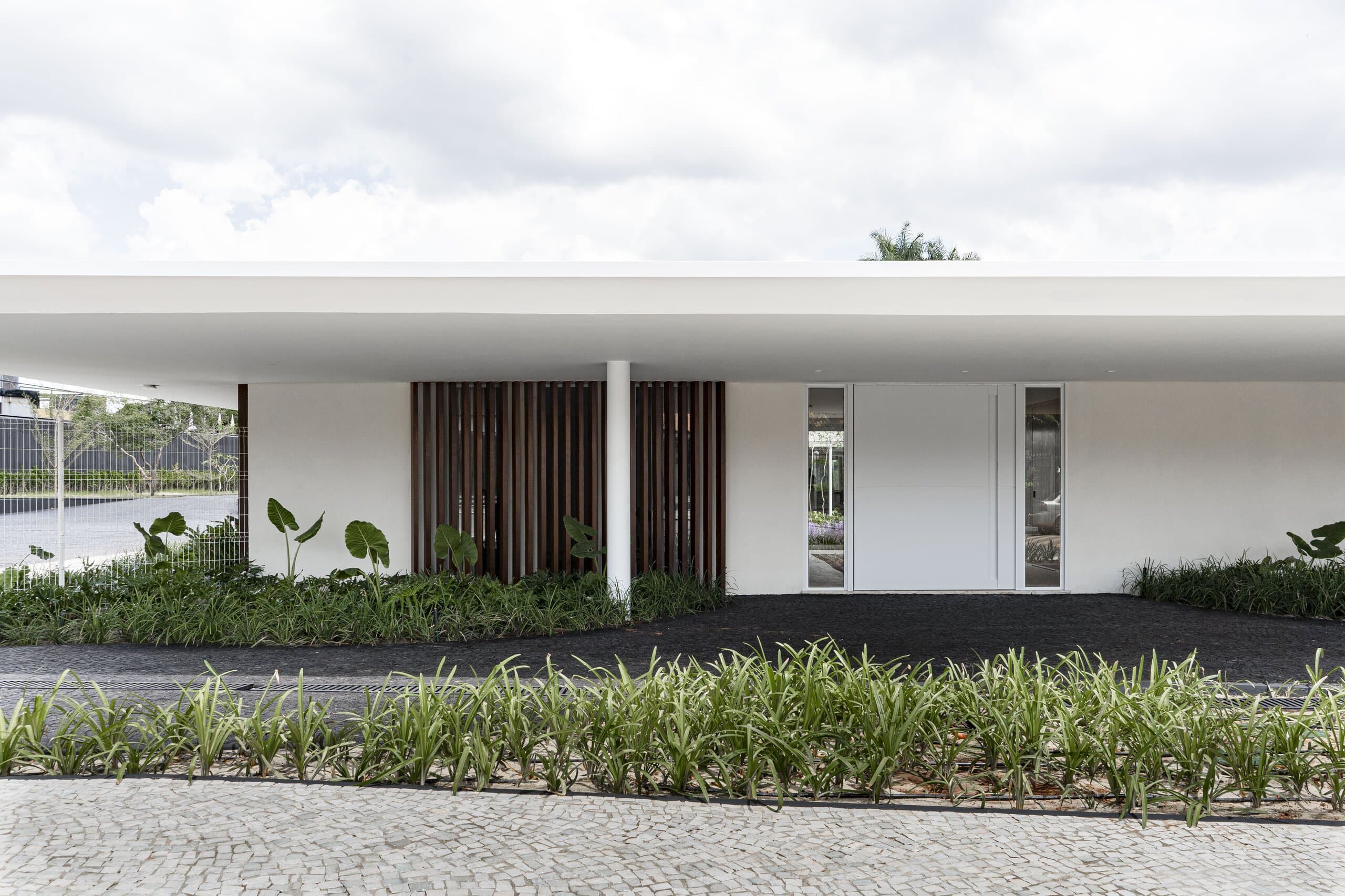 Closer on the façade: timber slats, a slim glazed slot and a strip of grasses along the cobbled kerb.