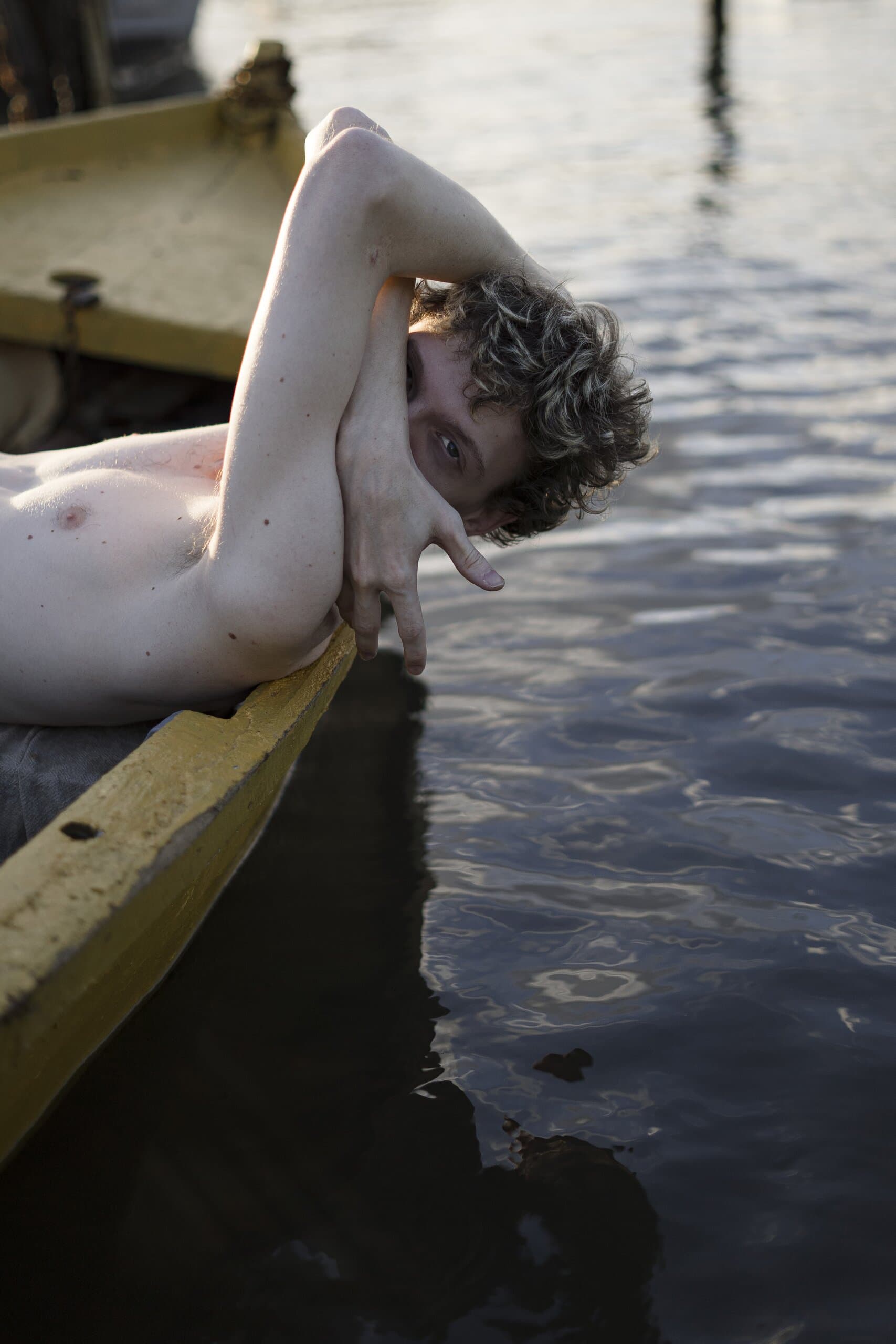 Leaning over the yellow gunwale, he hides his face in the crook of an arm, reflections of light on the water below.
