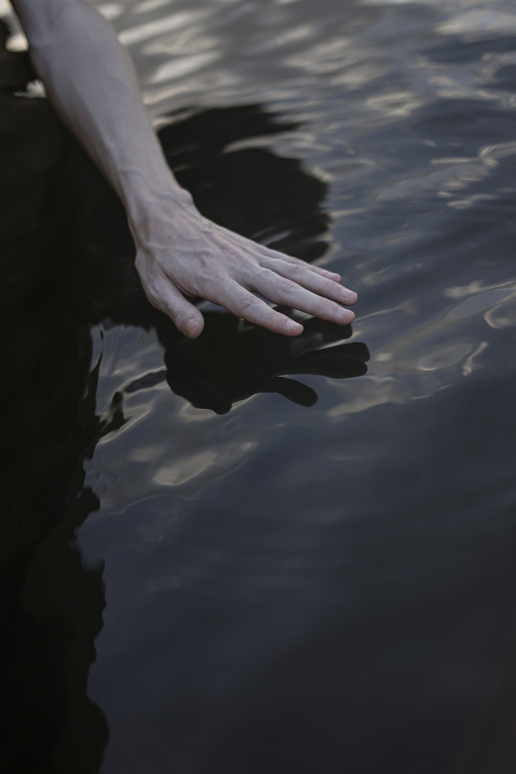 A hand spread flat on the surface of dark, rippling water.