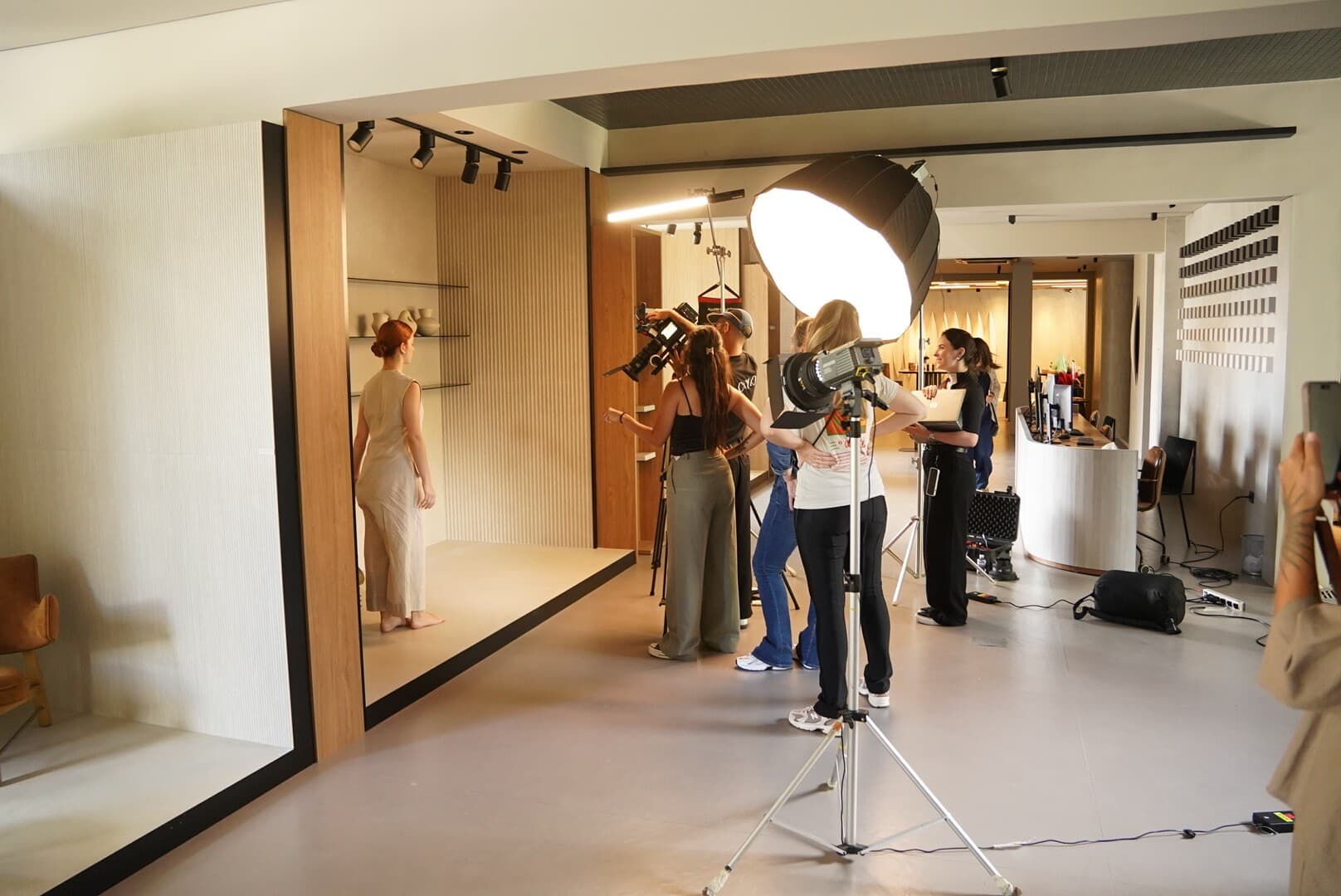No set, em estúdio: uma modelo num cenário de madeira enquanto a equipe ajusta as luzes e um grande softbox.