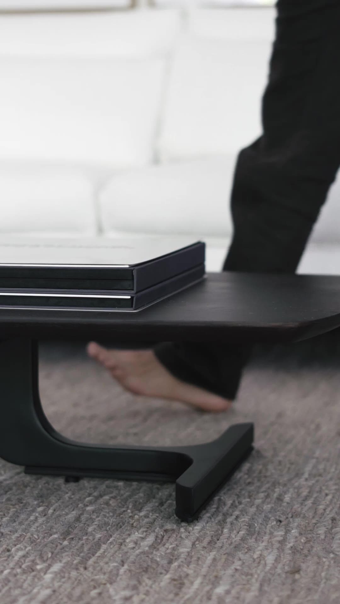 A Domus Mob reel: a bare foot steps past a dark timber table on a woven rug.