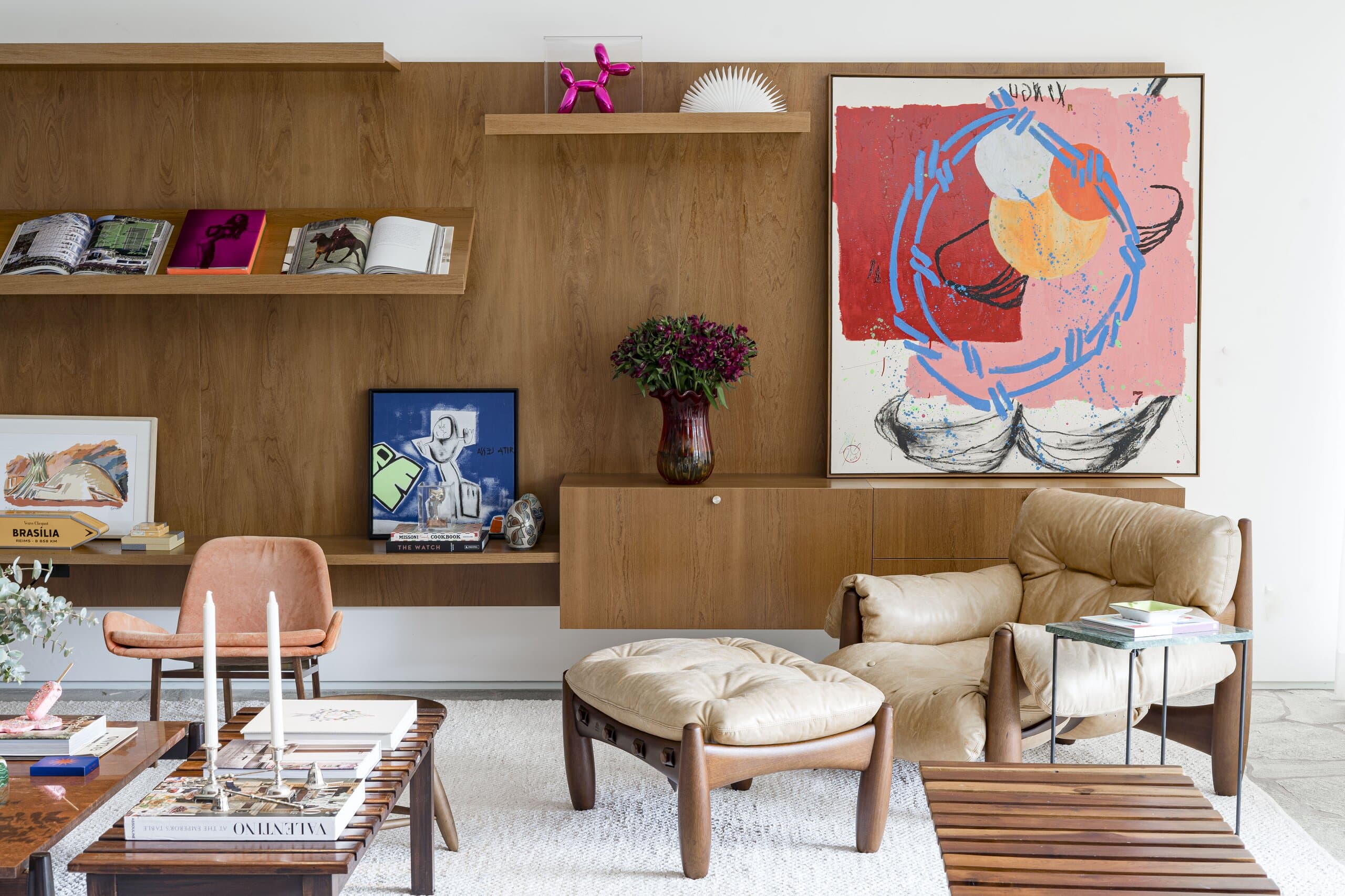 The red-and-blue painting above a leather armchair and footstool, a slatted timber bench and a candlestick on the coffee table.