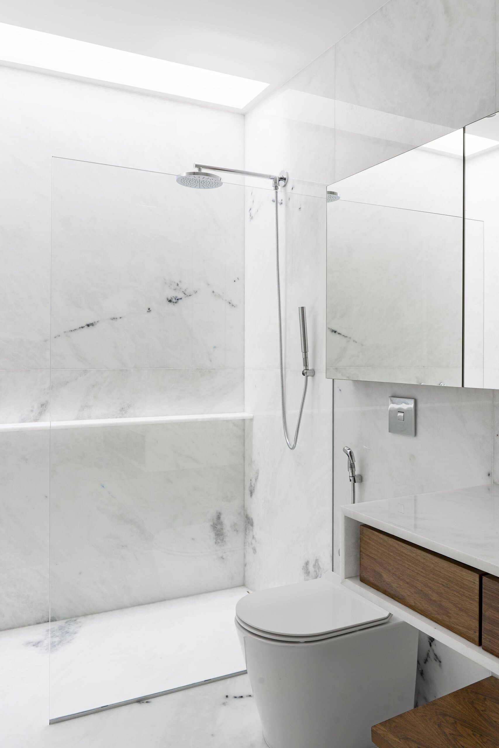 A white marble bathroom with a glass shower screen, a rain shower head and a timber vanity drawer.