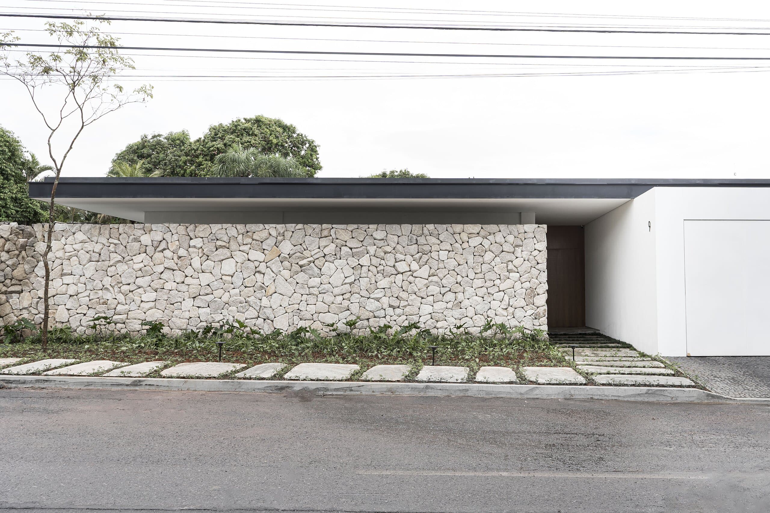 The street front: a low dry-stone wall beneath a thin flat roof, a white garage door and stepping stones set in grass.