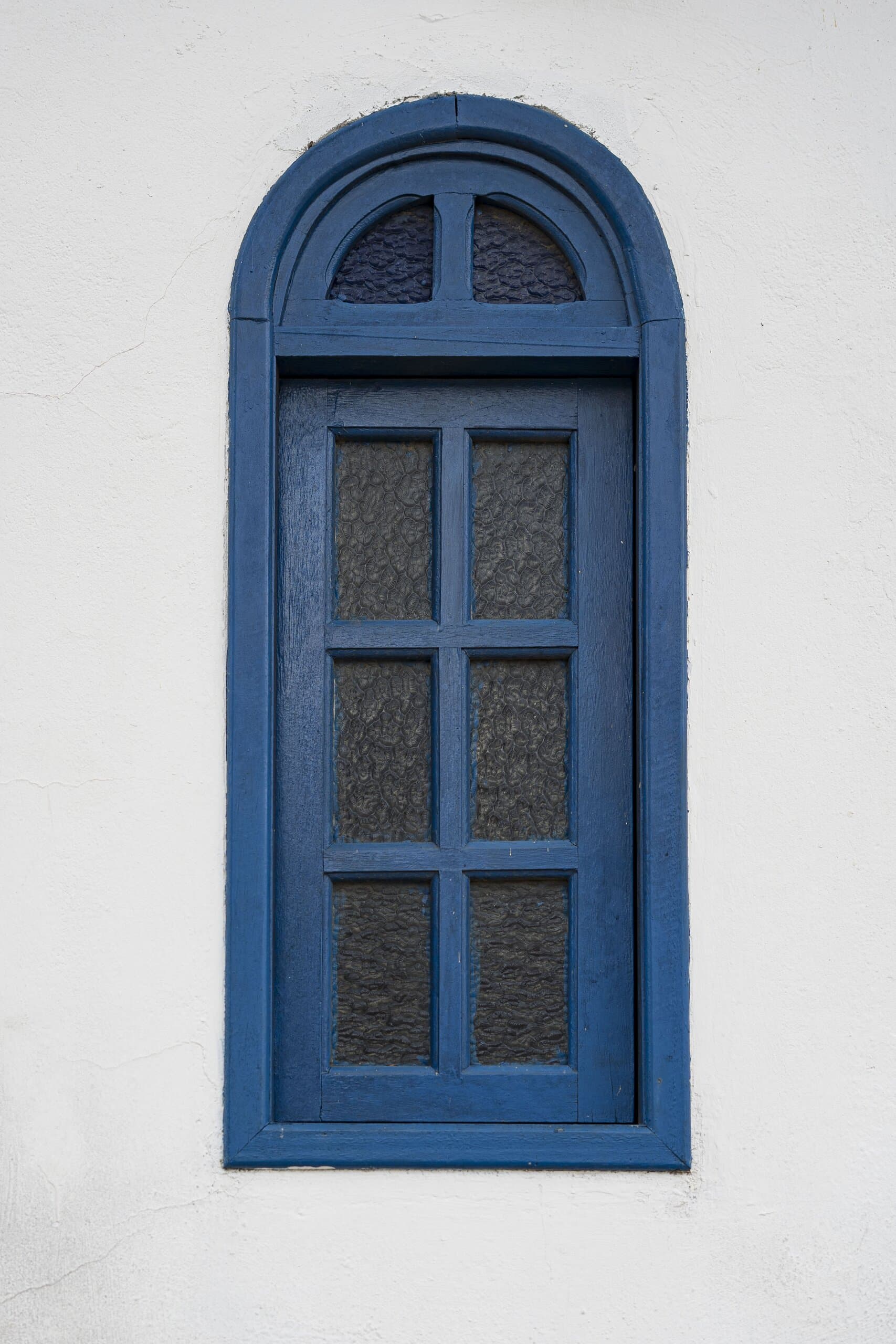 A blue timber arched window with frosted panes set in a white rendered wall.