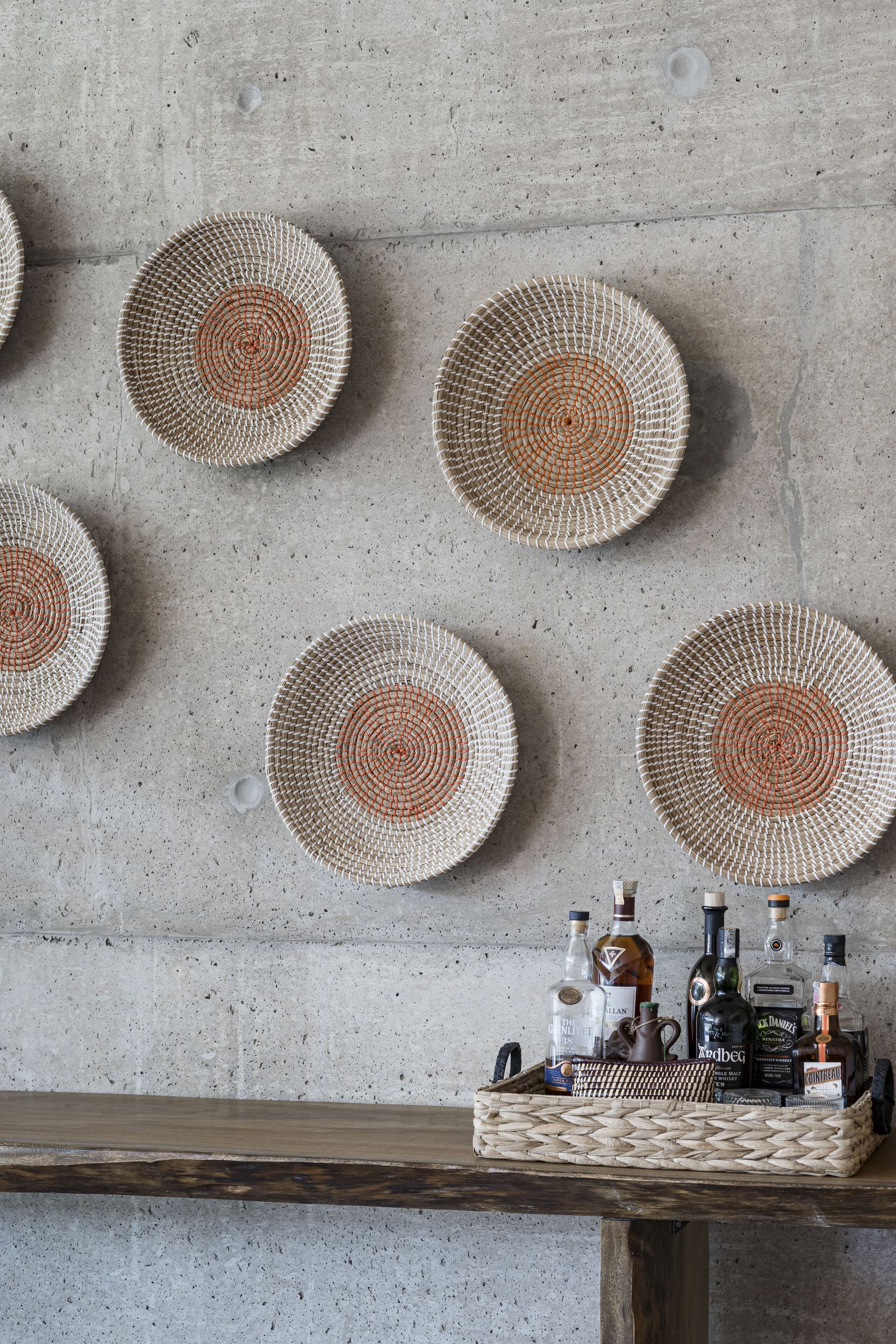 Woven baskets on a concrete wall above a bar of bottles.