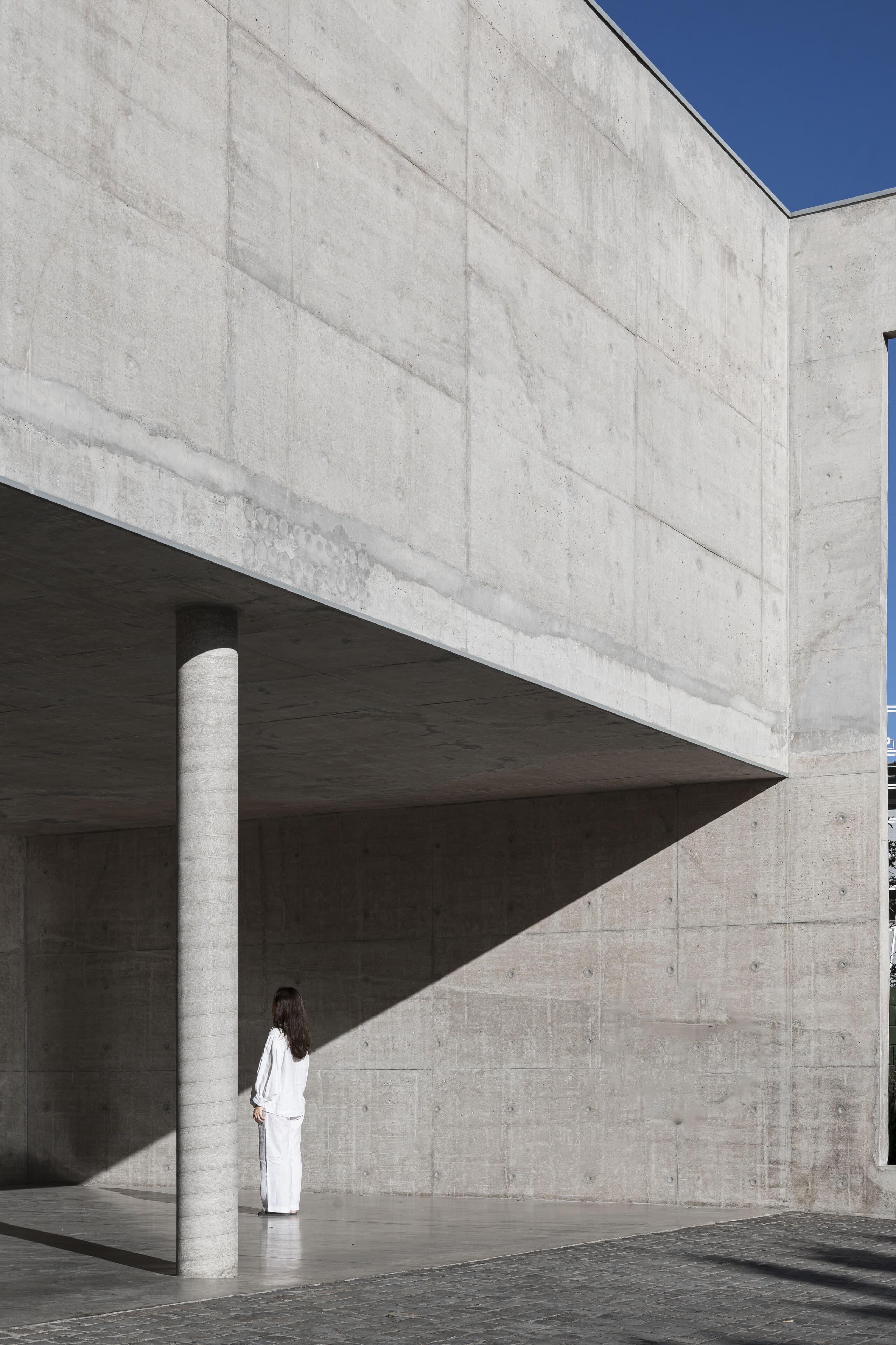 A woman in white beneath the cantilevered concrete volume, a single round column holding the edge.