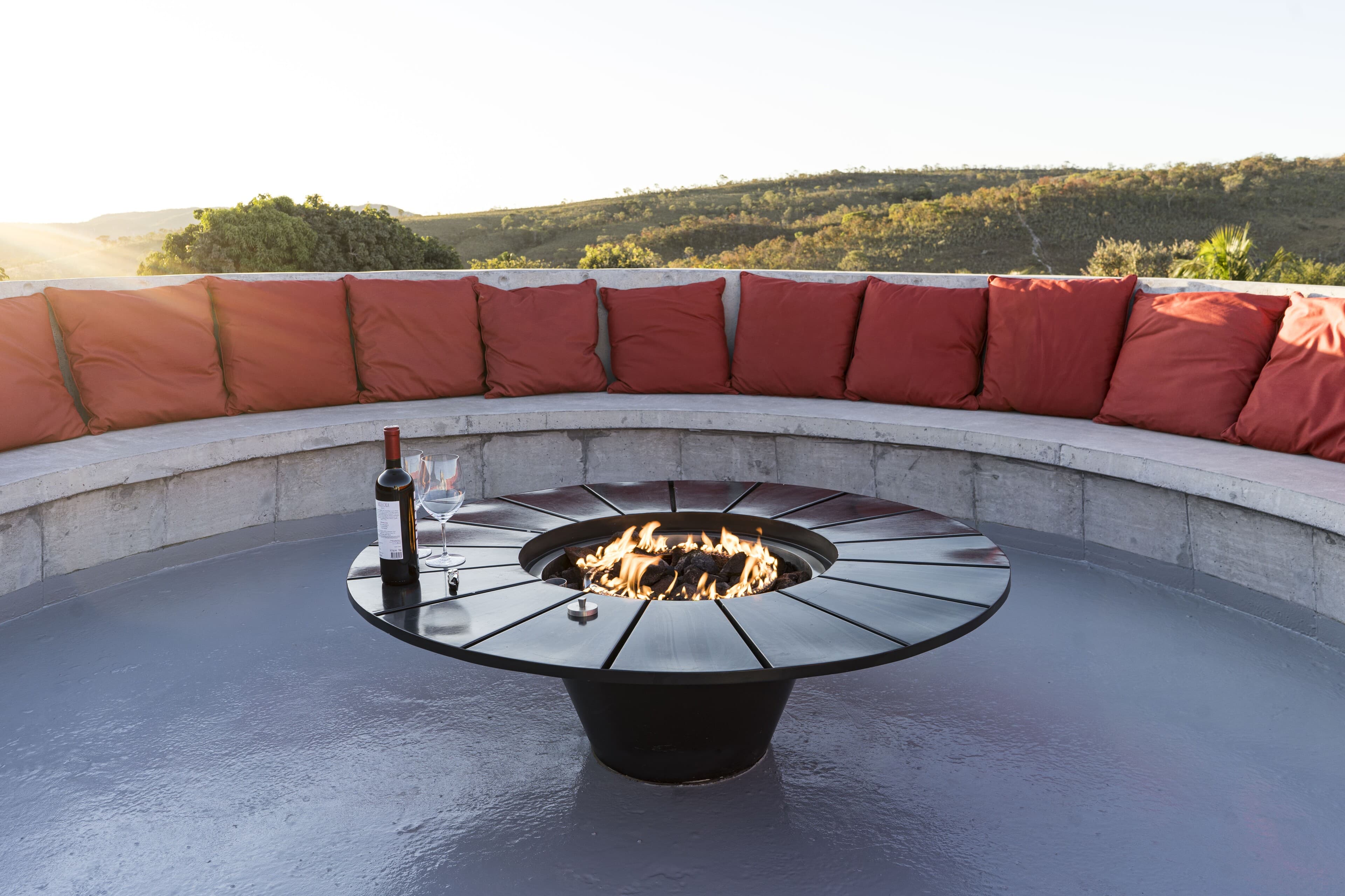 The sunken fire pit at golden hour: orange cushions, a bottle of wine and the hills beyond.